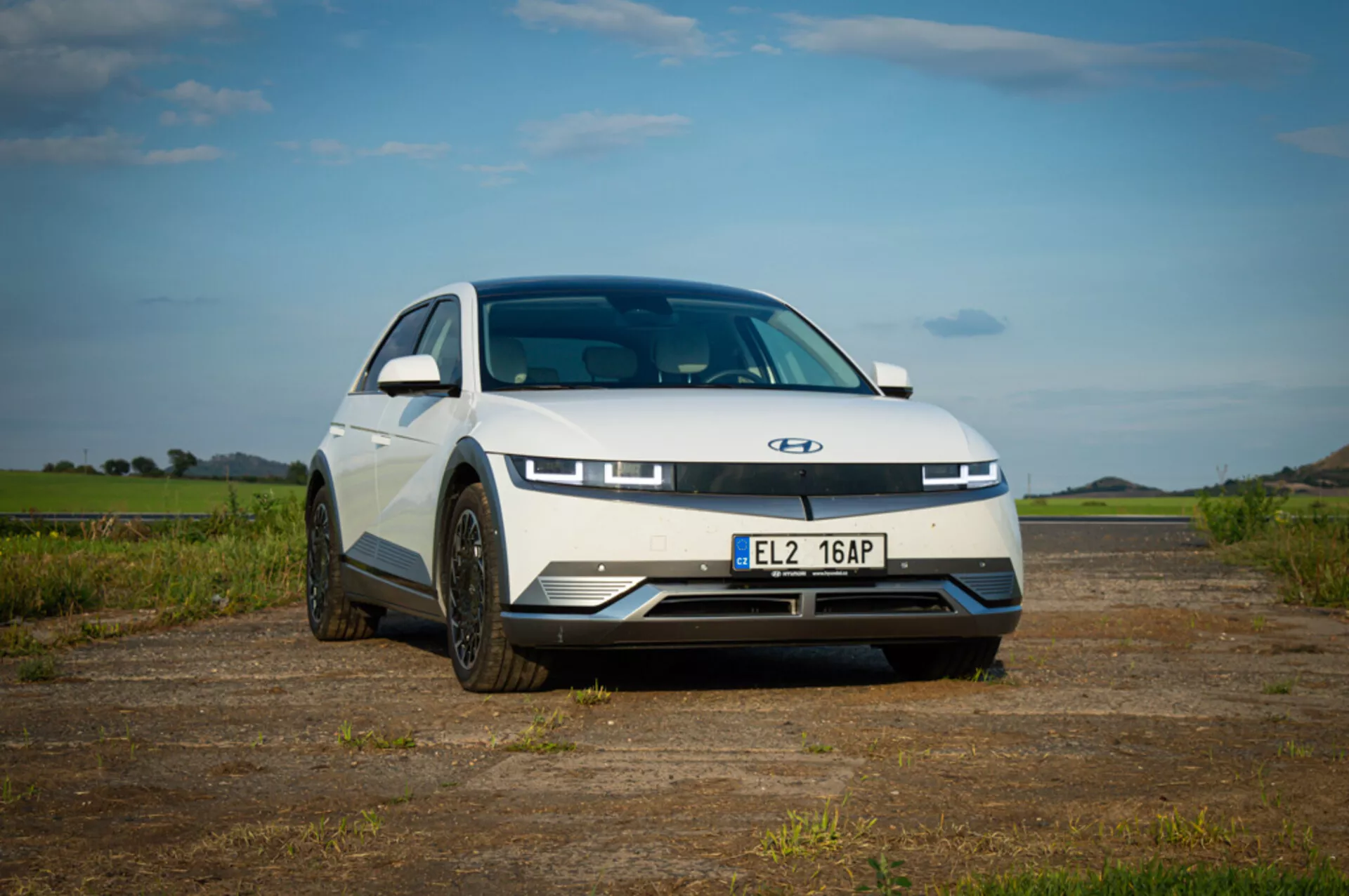 Hyundai Ioniq 5 elektrisk bil från 2021 som visar en modern design med elegant huva, distinkta LED-dagsljus, stängd frontgrill för aerodynamik och sportiga hjul, taget från ett lågt främre vinkel för att betona bilens främre stil och ställning, parkerad utomhus under en blå himmel