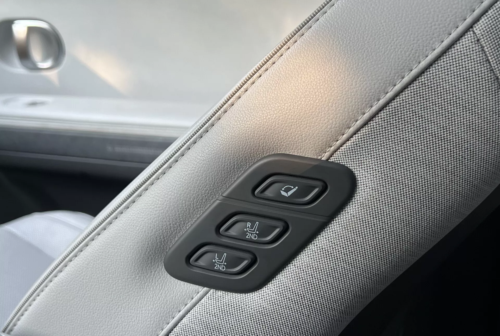 Detaljbild av interiören i Hyundai Ioniq-5 2021 med ljusgrå syntetisk eller läderklädsel med mörkgrå sömmar och kontroller för elektriska fönster och dörrlås på en pianosvart bakgrund