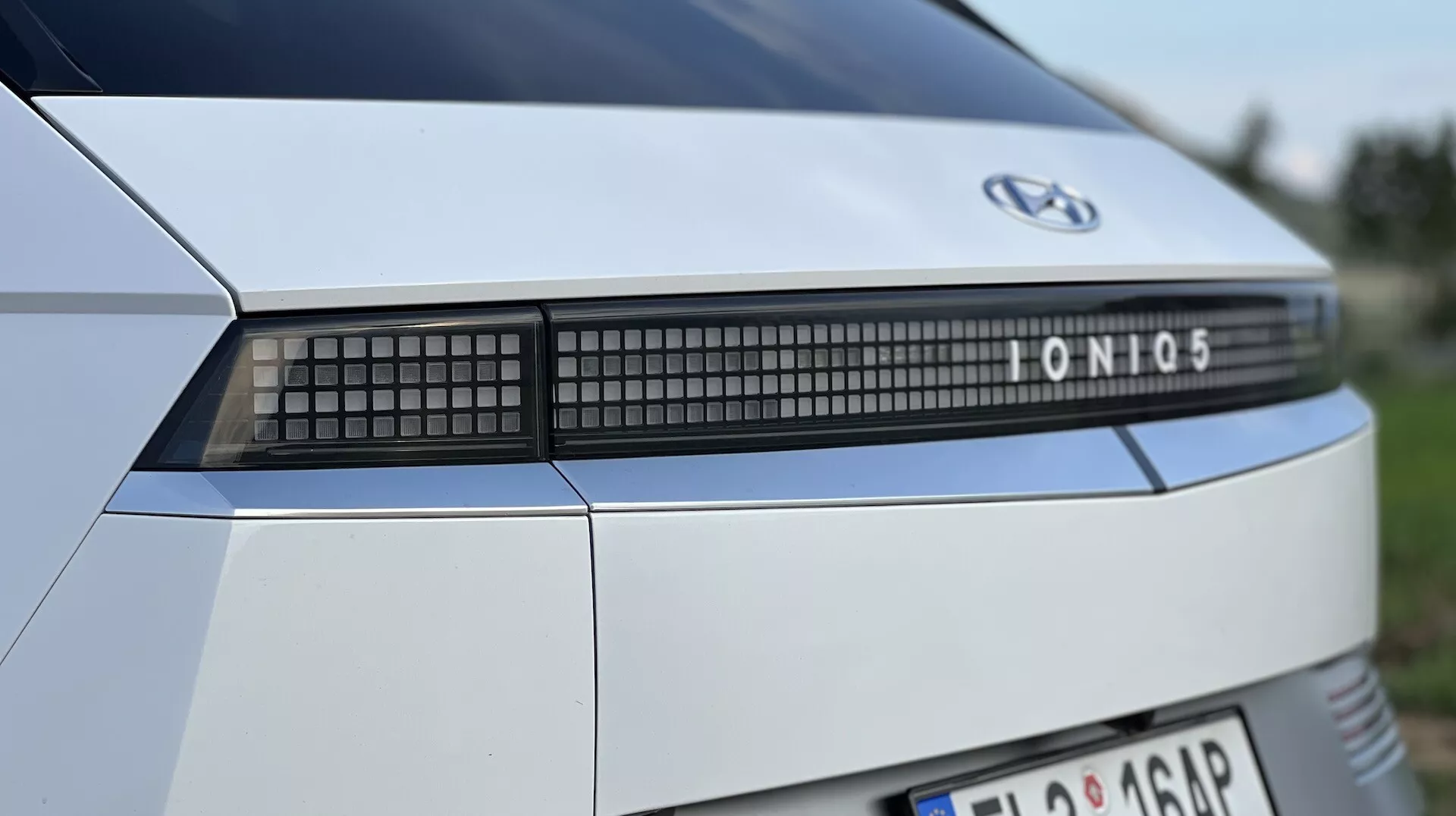 Närbild av bakändan på en Hyundai Ioniq 5 från 2021, som belyser varumärkets emblem, modellnamn och avancerad LED-ljusstav, mot en suddig utomhusbakgrund.