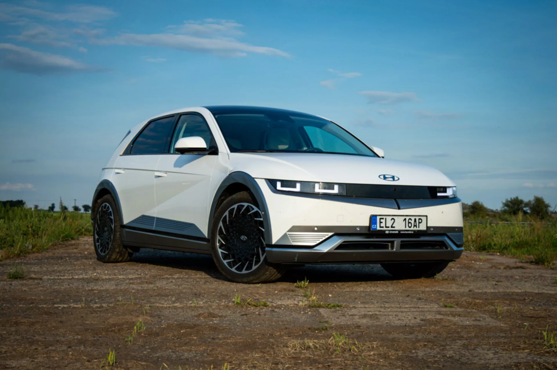Lågvinkelsvy av en Hyundai Ioniq 5 2021 som framhäver LED-strålkastare, aerodynamiska legeringshjul och slank kaross mot en bakgrund av jord och delvis molnig himmel
