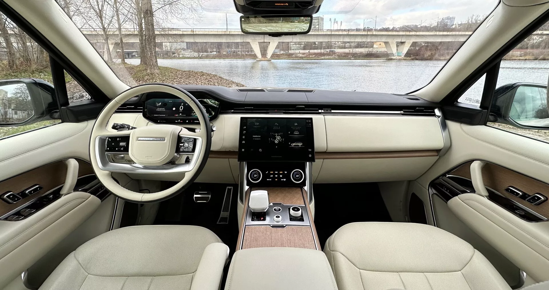 Interiörvy av Land Rover Range Rover 2021 från bakre sätena mot instrumentbrädan som visar symmetrisk design, ratt med multifunktionsknappar, pekskärms infotainmentsystem, digital klimatkontroll, lyxigt läderklädsel med trädetaljer och avancerade tekniska funktioner