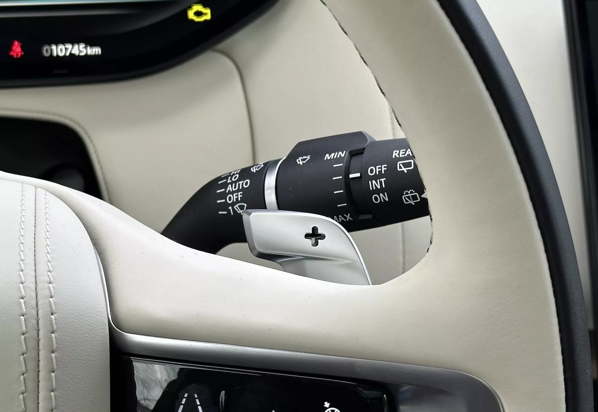 Närbild inuti Land-Rover Range-Rover 2021 som visar ratten kolumnen, vindrutetorkarens kontrollspak med flera inställningar inklusive OFF, INT, ON, hastighetsjusterare och AUTO för automatiska regnsensande vindrutetorkare, plus ett bakre torkaralternativ. Synlig del av instrumentpanelen visar 10745 km, satt mot en premium svart och kräm interiör.