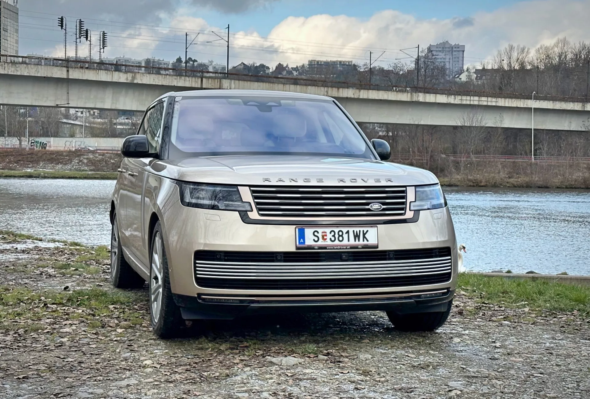 Lyxig SUV Range Rover 2021 parkerad utomhus nära en flod och bro i en urban miljö, visar sin moderna design, främre grill och eleganta LED-strålkastare