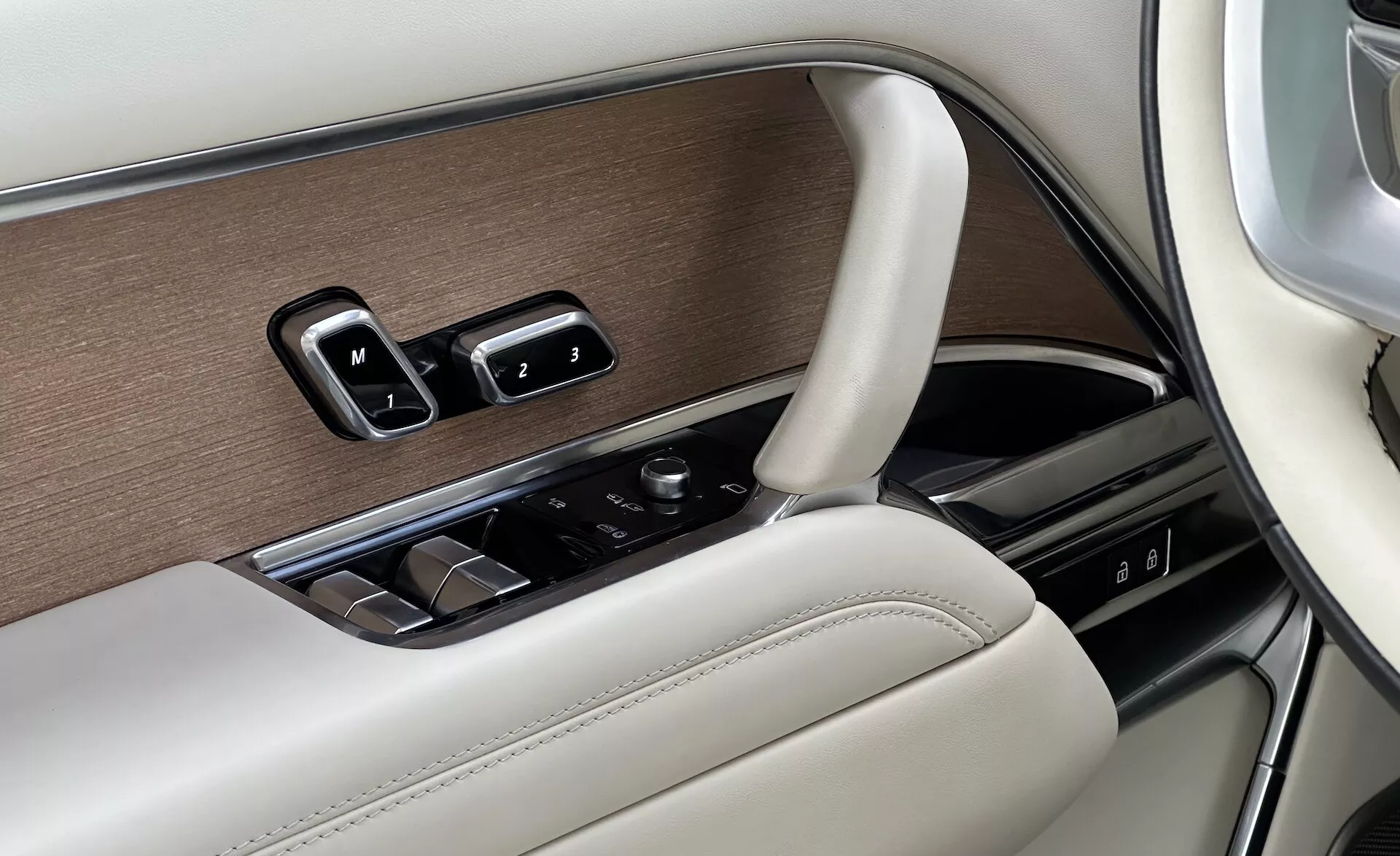 Detalj av interiören i en Land Rover Range Rover 2021 som visar förarsidans dörrpanel med fönsterkontroller, spegeljusteringar, minnessätesinställningar i en lyxig design med träfanér, krom och läderavslutningar, samt en kontrollknapp för infotainmentsystemet.