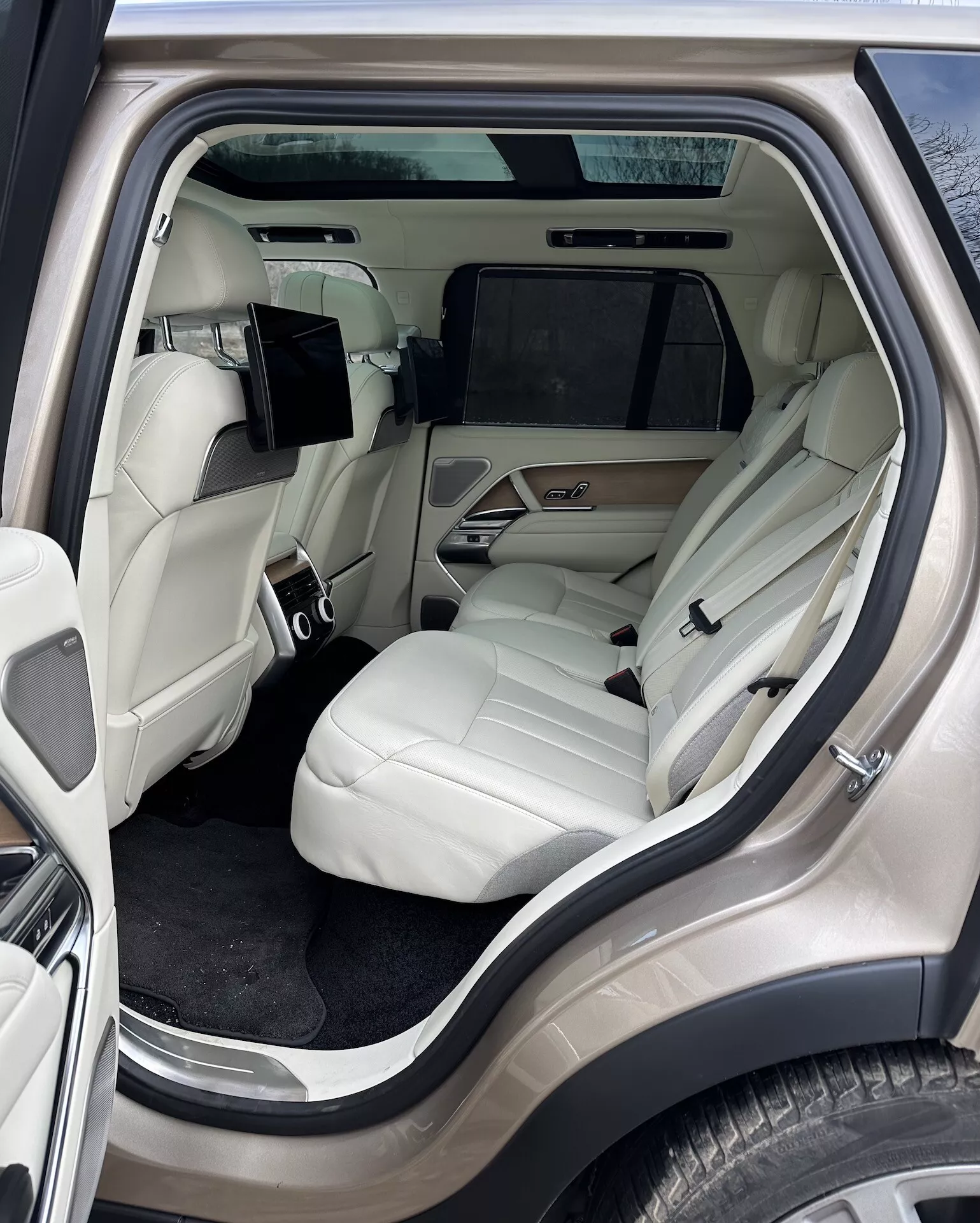 Interiörvy av Land Rover Range Rover 2021 med fokus på det lyxiga baksätesutrymmet från en yttre sidovinkel, med ljusfärgade lädersäten, avancerad mittkonsol, underhållningssystem och lyxdetaljer
