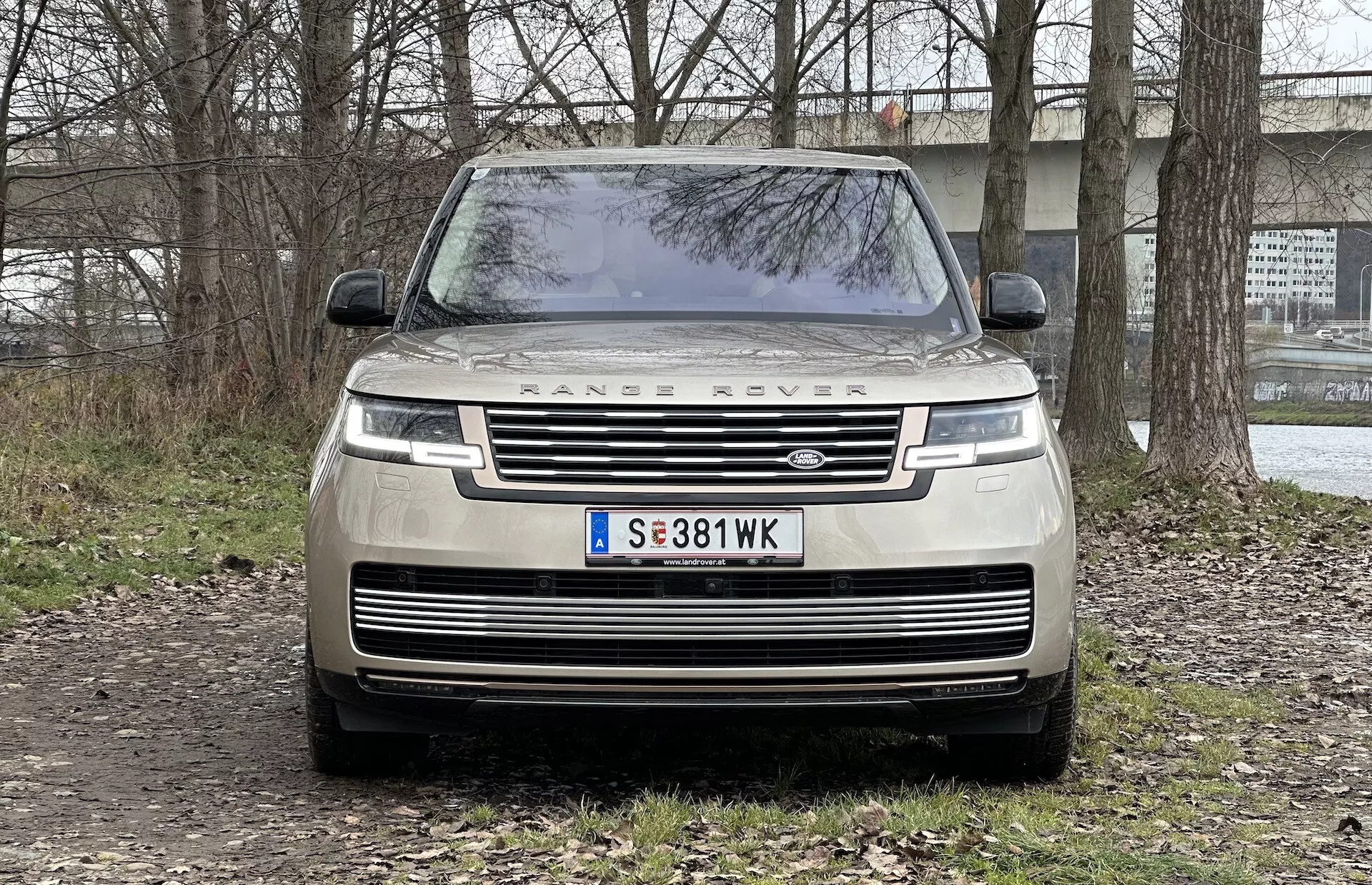 Framifrån vy av en 2021 Range Rover som visar grillen, LED-strålkastare, 'RANGE ROVER' bokstäver på huven och parkerad på en oasfalterad yta med en halvt landsbygd bakgrund