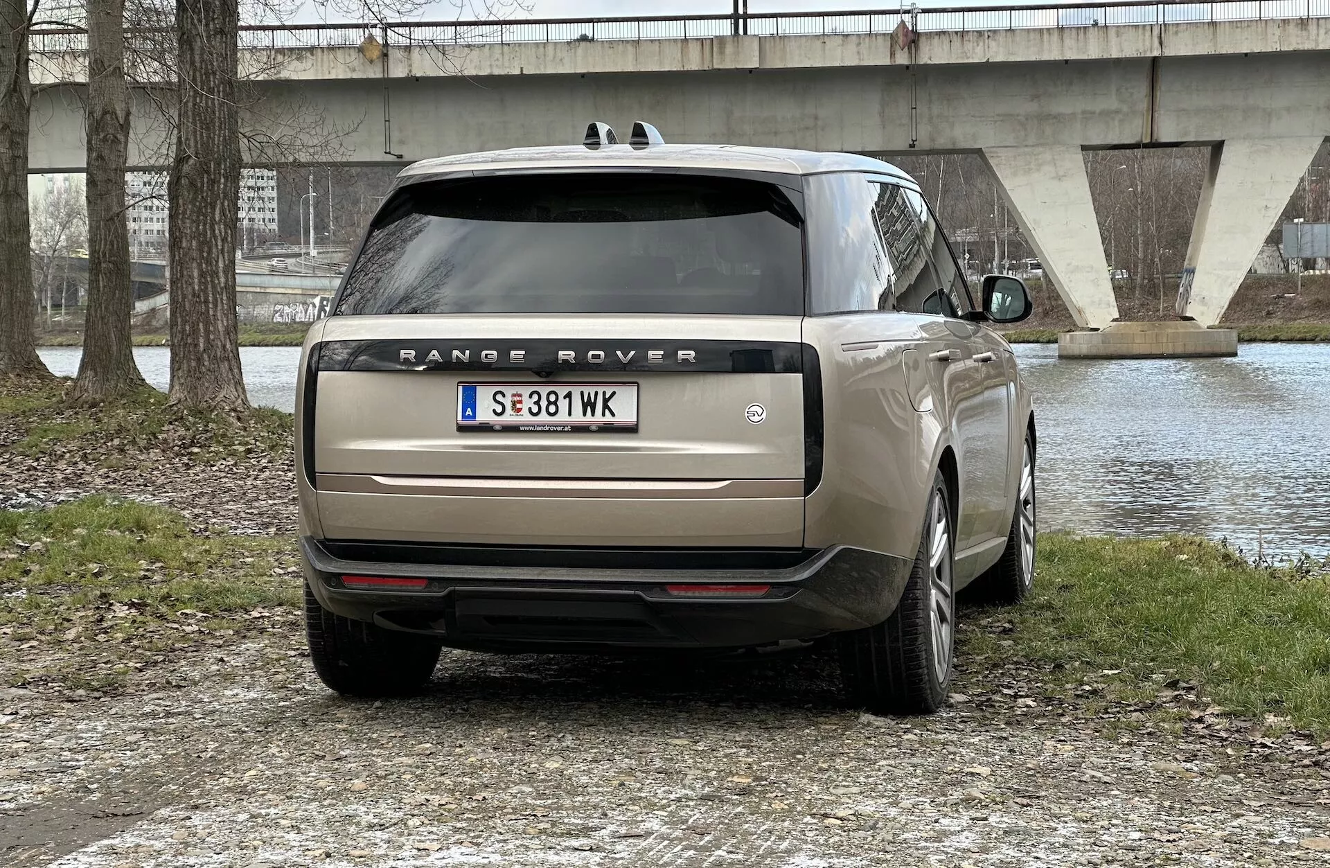 Baksida av en Range Rover 2021 parkerad utomhus med vattenkropp och bro i bakgrunden, som visar LED-bakljus, dubbel avgas, tonade rutor och flerstråliga legeringshjul.