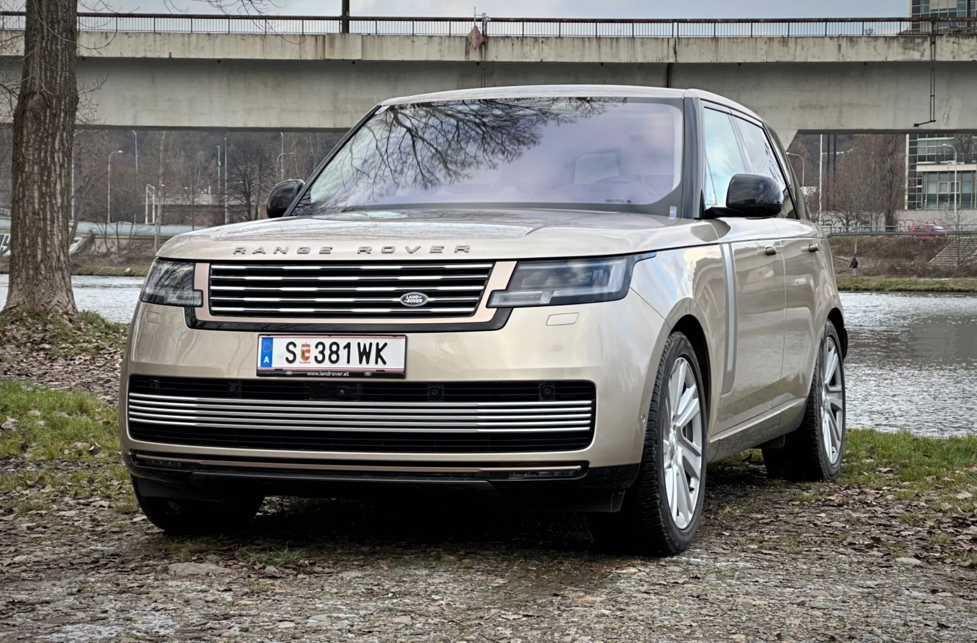 Range Rover 2021 i ett slående framifrån-tre fjärdedels perspektiv som visar dess distinkta grill, slanka LED-strålkastare och robusta frontplåt mot en stads park bakgrund, vilket betonar lyx och terrängkapacitet.
