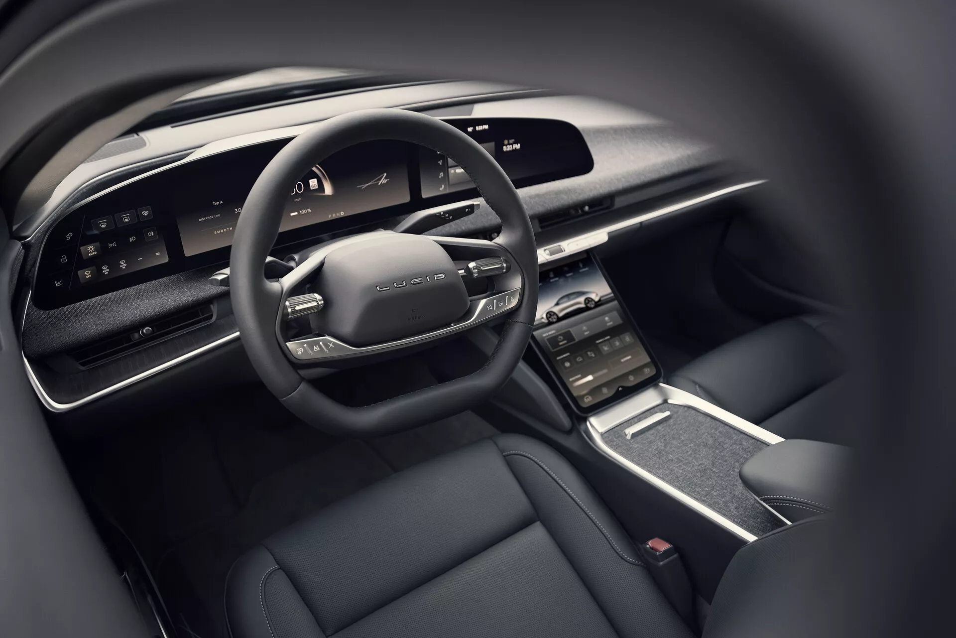 Närbild av Lucid Air 2022 förarens cockpit från baksätets perspektiv, som visar den moderna multifunktionsratten med kontroller, bred digital instrumentpanel, vertikalt orienterad mittpekskärm med omgivande luftventiler, elegant mittkonsol med minimalt antal fysiska knappar och en lyxig interiör med mörkt färgschema som innehåller material av hög kvalitet.