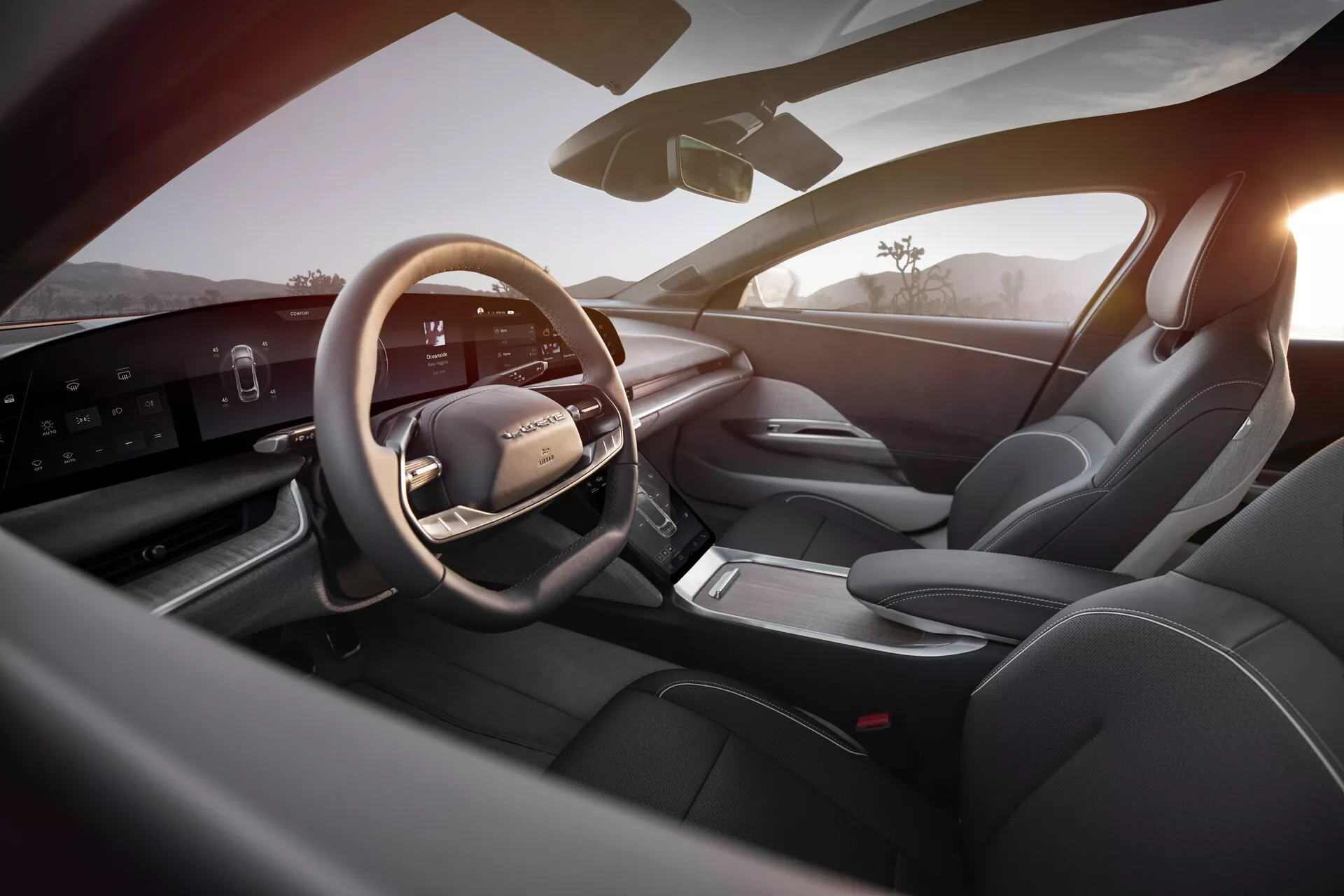 Interiör vy av 2022 Lucid Air, som visar ett lyxigt och modernt förarområde från perspektivet av baksätet till höger. Höjdpunkter inkluderar en läderklädd, multifunktionell ratt med monterade kontroller, en elegant horisontell digital instrumentpanel, en strömlinjeformad mittkonsol med minimala knappar och elektronisk växelväljare, sportiga säten klädda i läder, sofistikerade dörrpanelkontroller och god sikt totalt sett med en sidospegel och vindruta. Den väl upplysta interiören framhäver den banbrytande teknologin och den sofistikerade designen, förstärkt av det varma utomhusljuset som antyder soluppgång eller solnedgång.
