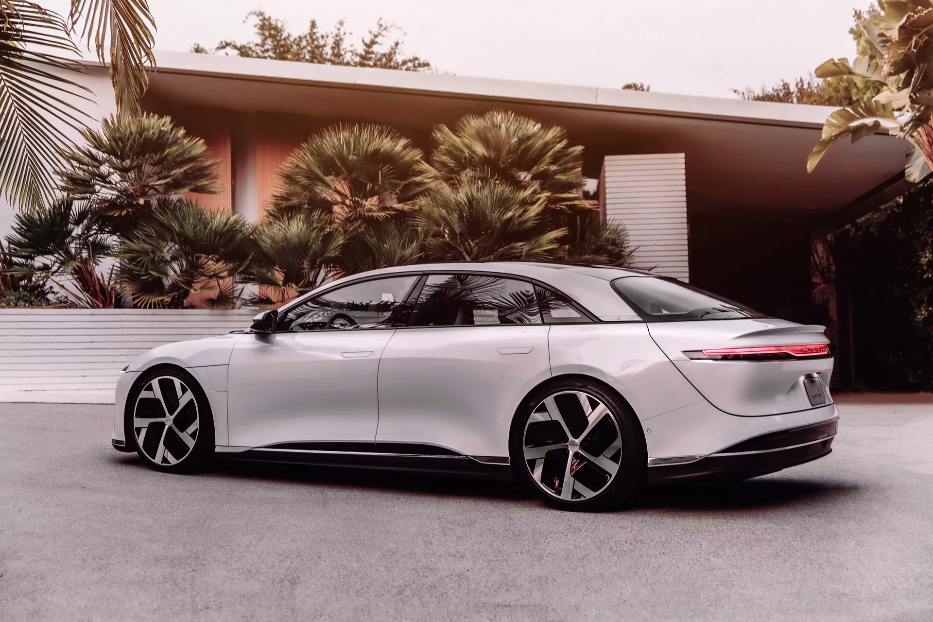 2022 Lucid Air elektrisk sedan, 1:a generationen, sidoprofil sedd från en låg vinkel som betonar den aerodynamiska designen, eleganta LED-strålkastare, slätt framskärm, infällda utdragbara dörrhandtag, tvåfärgade fem-ekrade lättmetallfälgar, tonade fönster, fastback-bakdel med horisontell ljusremsa och integrerad spoiler, som visar modern teknik och design för elfordon.