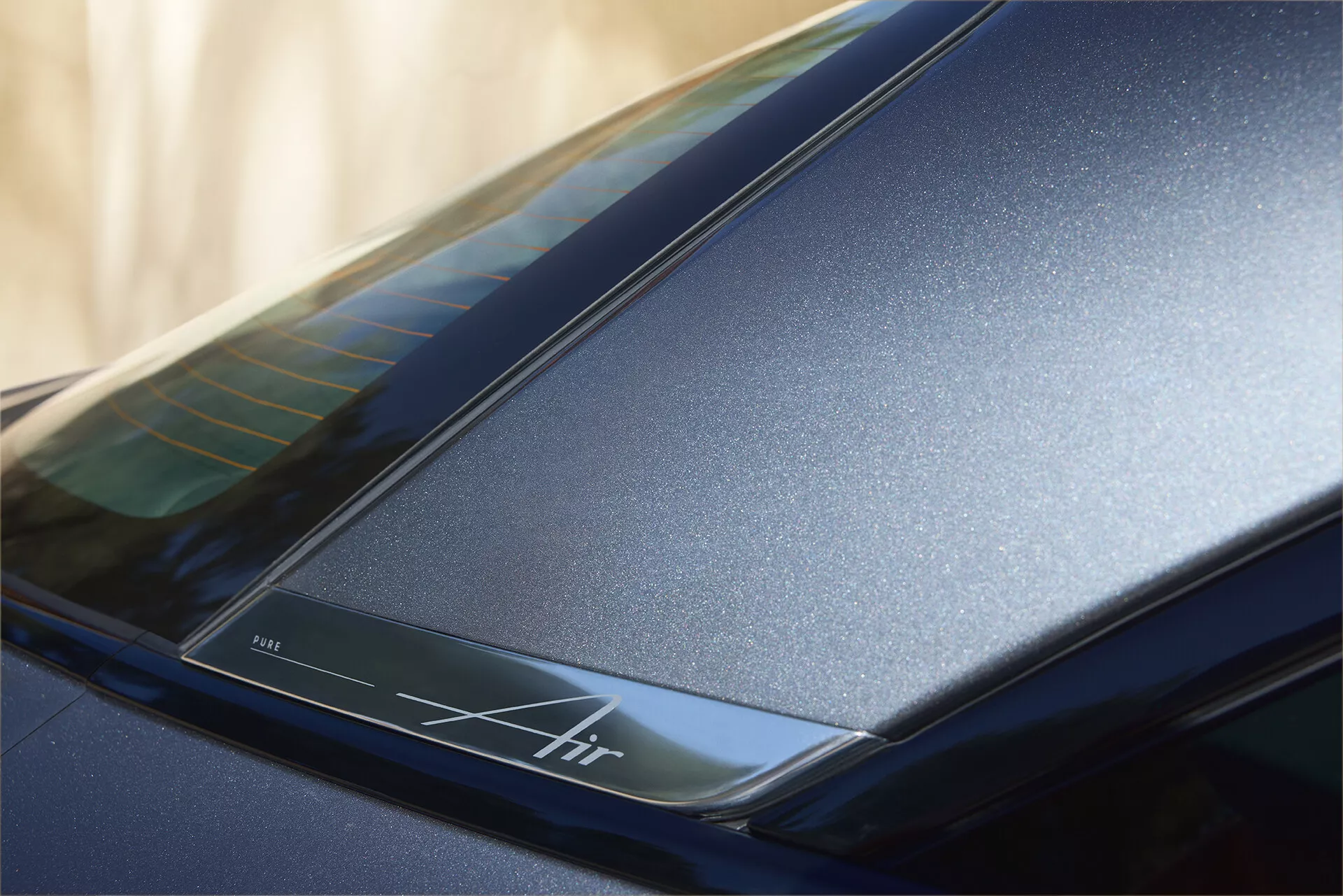 Närbild av bakre sektionen nära taket på en Lucid Air 2022 (1:a generationen), som framhäver den mörkblå glansiga finishen och de eleganta aerodynamiska linjerna. Innehåller en bakgrundsbelyst remsa med inskriptionen 'Air', vilket betonar lyxdesign och eventuell avancerad teknik.