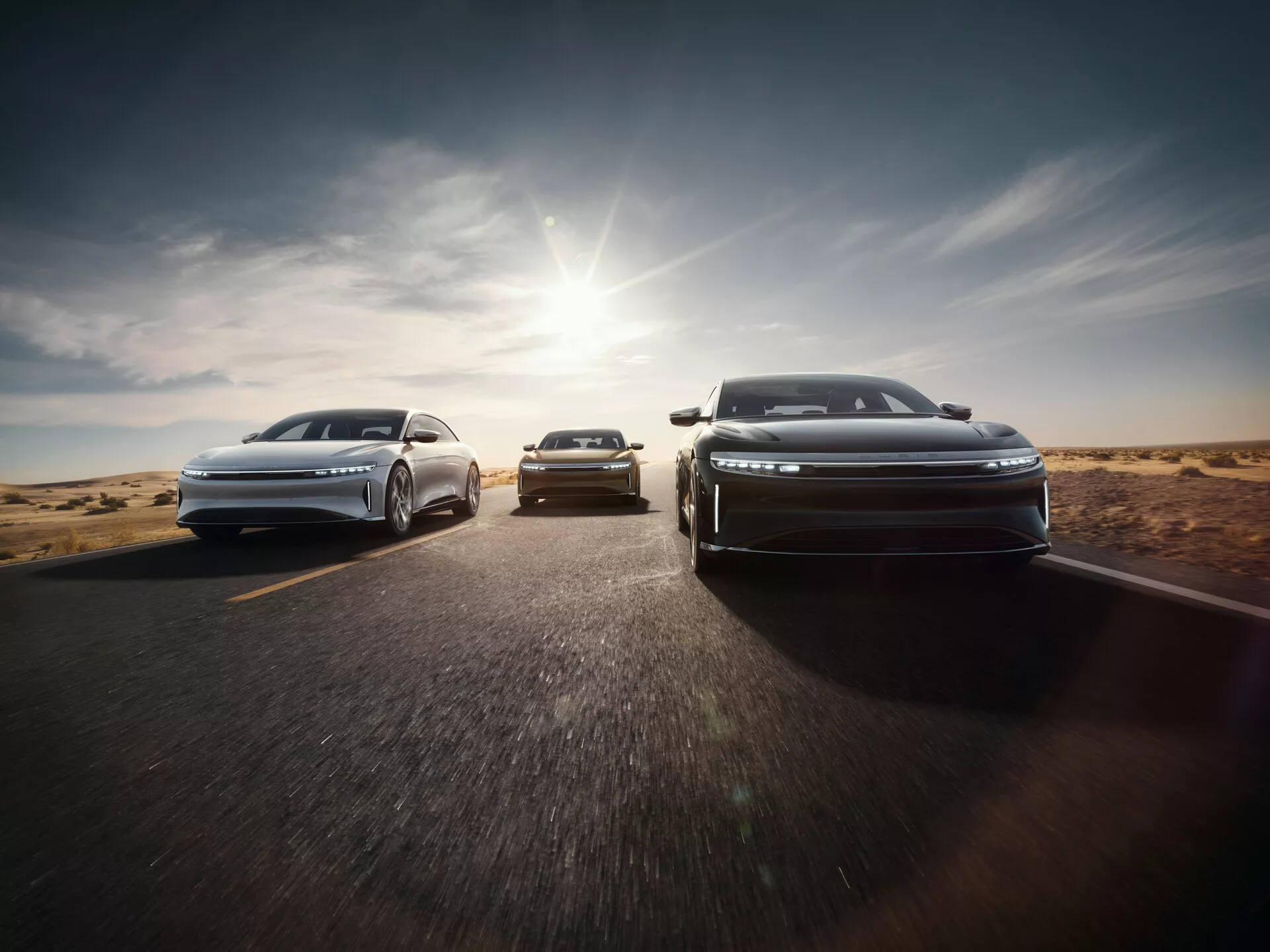 Främre vy av Lucid Air 2022 med aerodynamisk design och LED-strålkastare i stegvis formation på asfaltsväg med ökenbakgrund, solljus som kastar varm glöd