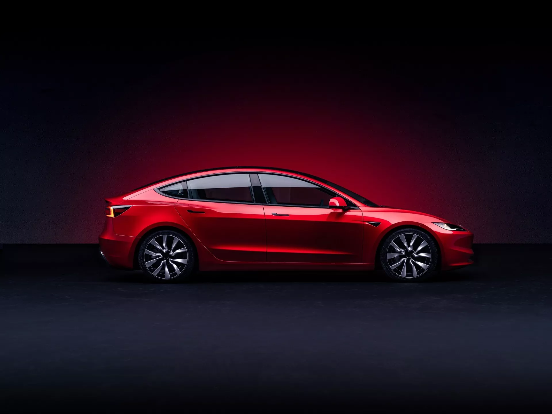 Facelift av första generationens Tesla Model 3 2023, röd sedan med panoramatak och LED-belysning, sidoprofil i studio med mörk gradientbakgrund, utrustad med legeringshjul och avancerad teknik för elbilar