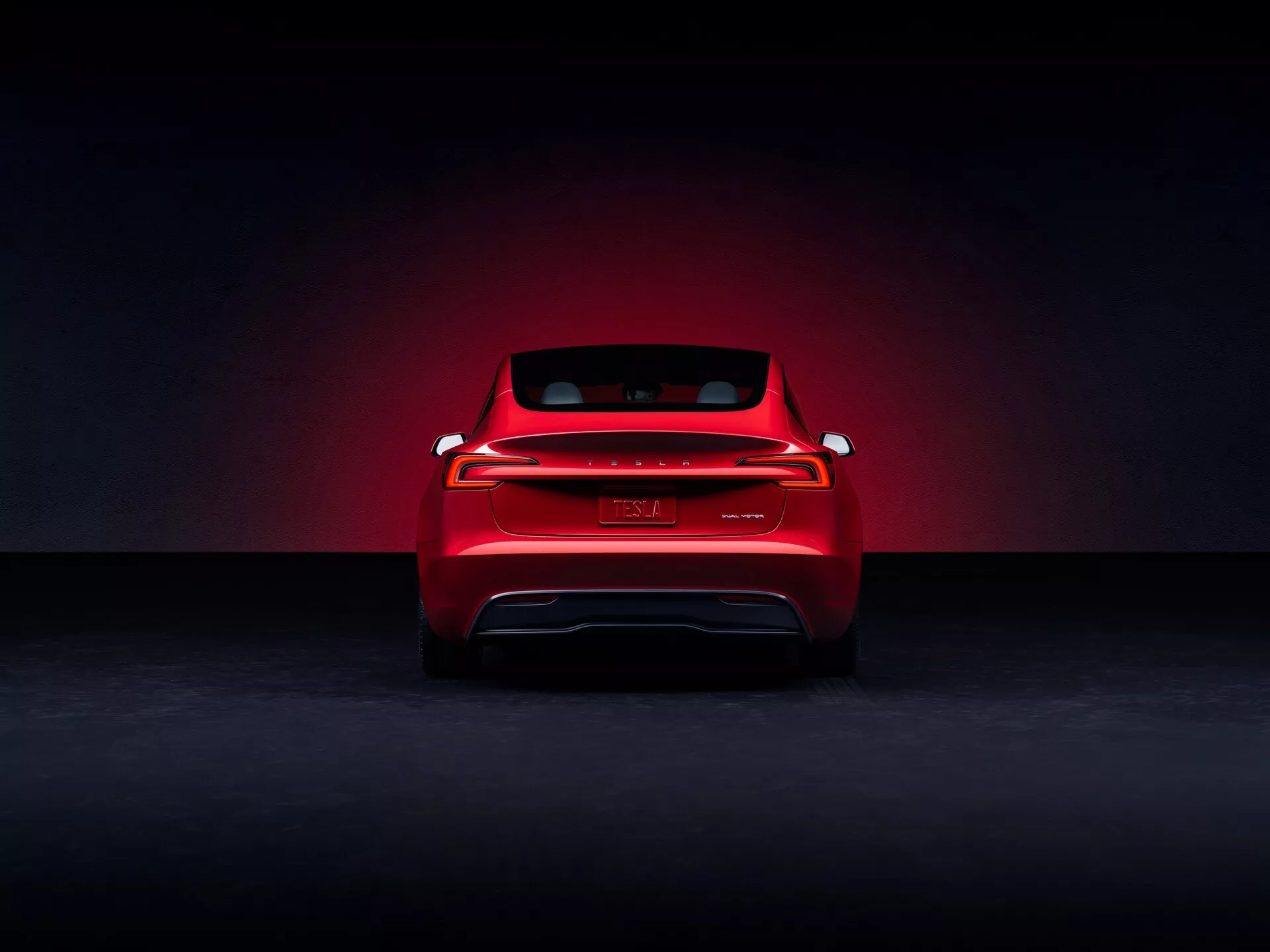 Tesla Model 3 2023 (första generationens ansiktslyftning) presenterad från ett bakre, reklammässigt perspektiv i studiomiljö, med röd lackfinish och dramatisk strålkastarhaloeffekt, som visar dess moderna LED-bakljus som sträcker sig över bredden, emblem utan synlig branding, antydningar till elektriskt fordon utan avgas, och en sportig bakrutans siluett.