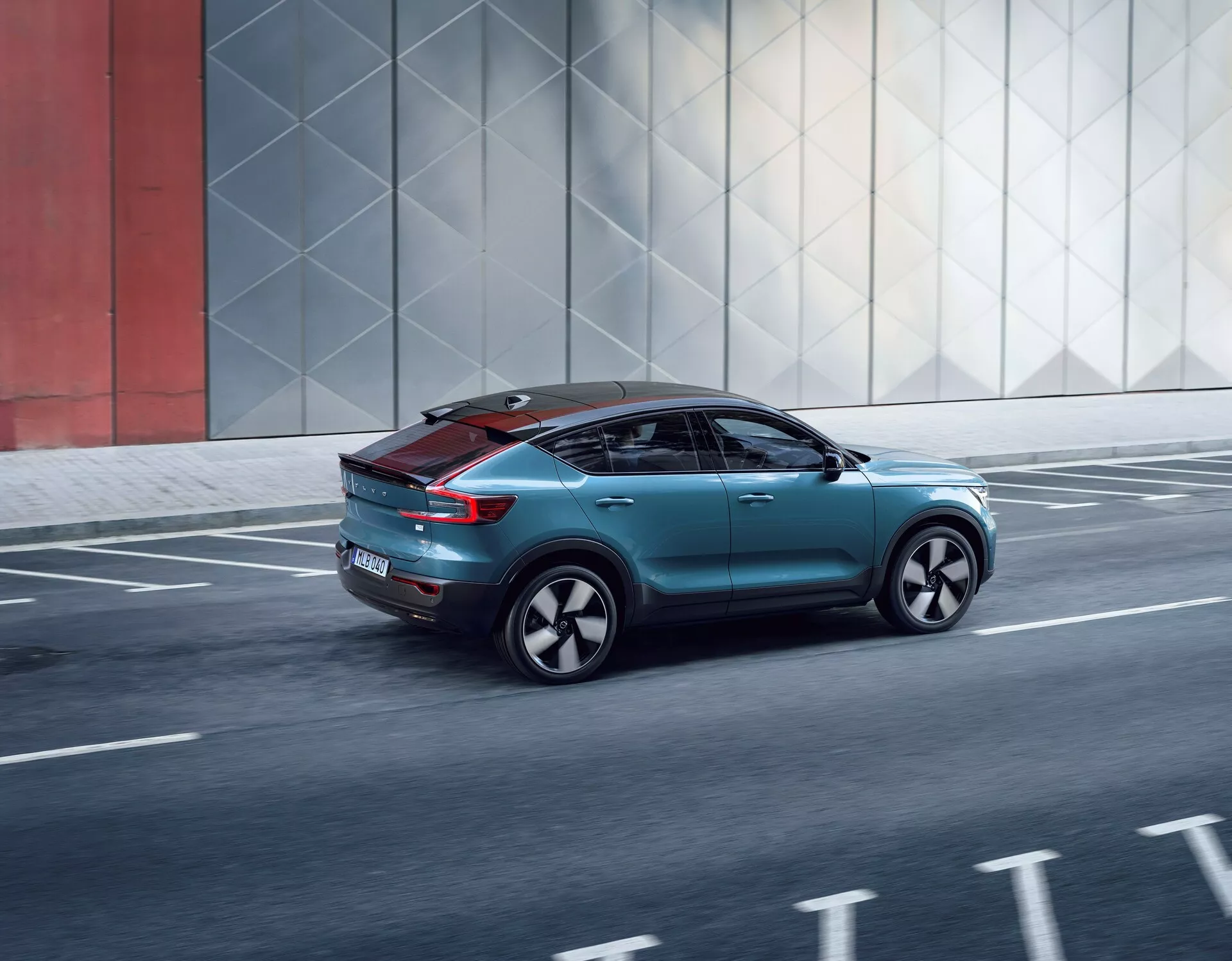 Dynamisk trekvart bakifrån av Volvo C40 2021, som visar dess eleganta design, aerodynamiska detaljer, moderna bakljus, skräddarsydda hjul och panoramatak, när den rör sig längs en stads väg.