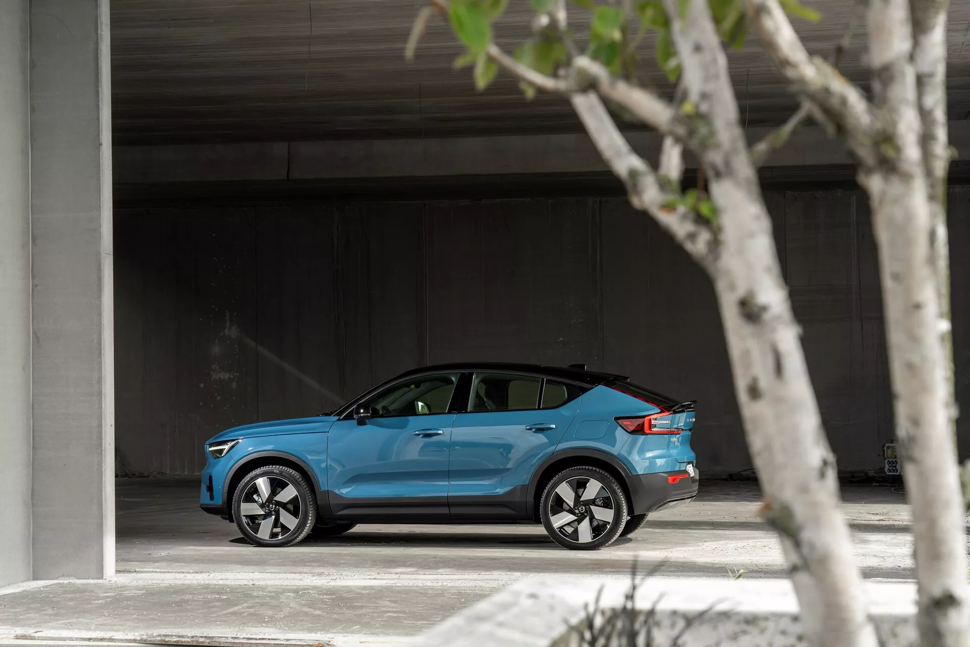 Sidoprofil av en ljusblå 2021 Volvo C40 parkerad i ett rymligt område, som visar upp sin eleganta, moderna design, silverfärgade flerspinnade aluminiumfälgar, lätt tonade fönster och en potentiell laddportslucka.