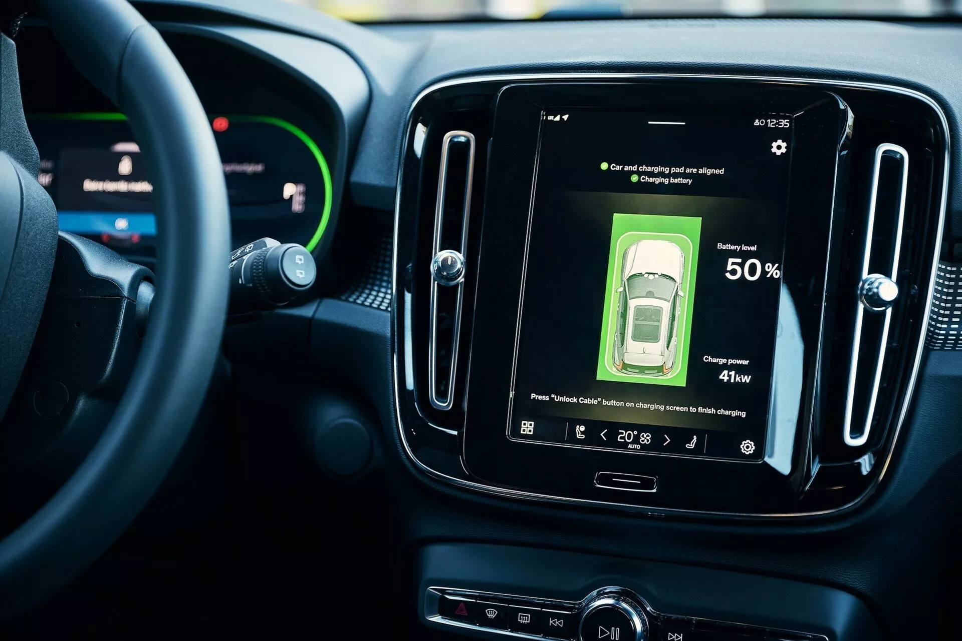 Interiörvy av ett modernt fordon med fokus på det centrala infotainmentsystemet. Delvis synlig ratt med digital instrumentpanel och synlig central pekskärm som visar bilens status med 50% batterinivå och 41kw laddningseffekt. Indikatorer visar '88' och '20:13'. Högupplöst skärm exemplifierar modern fordonsteknik i elbilar, med fokus på anslutning och användarvänligt gränssnitt. Modern instrumentbräddesign.