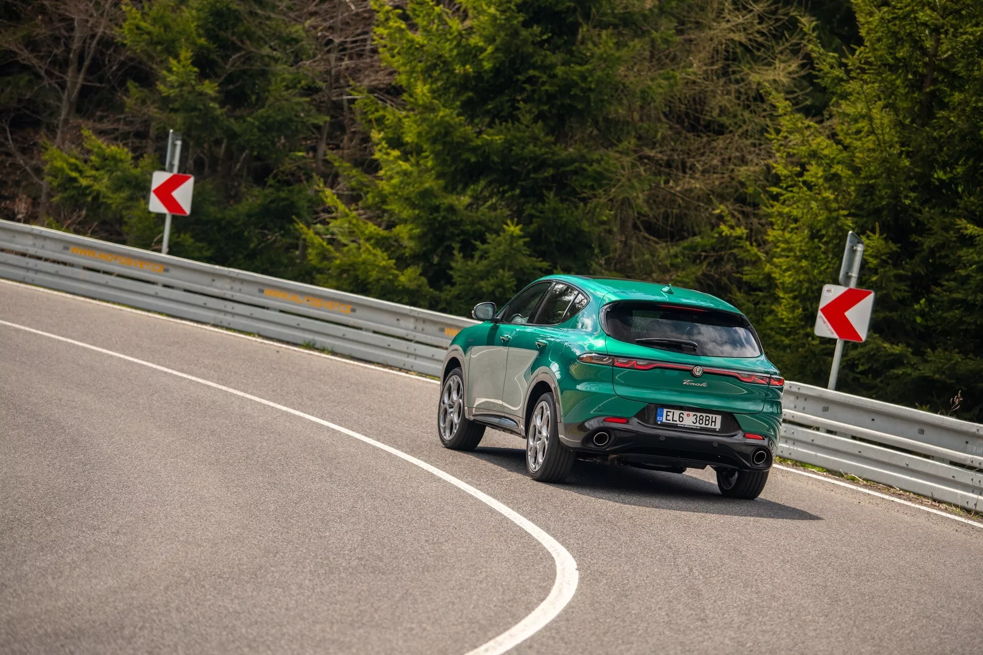 Alfa Romeo Tonale 2022 fångad från en tre fjärdedels vinkel bakifrån på en kurvig väg, med betoning på dess sportiga halvkombi design, glansig finish och aerodynamiska egenskaper inklusive en bakre spoiler, legeringshjul och LED bakljus.