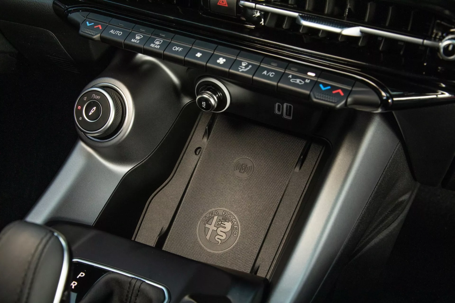 Närbild av mittkonsolen i Alfa Romeo Tonale 2022, med visning av klimatkontrollpanel, trådlös laddningsplatta, växelspak och infotainmentkontrolldial med premiumfinish och modern design.