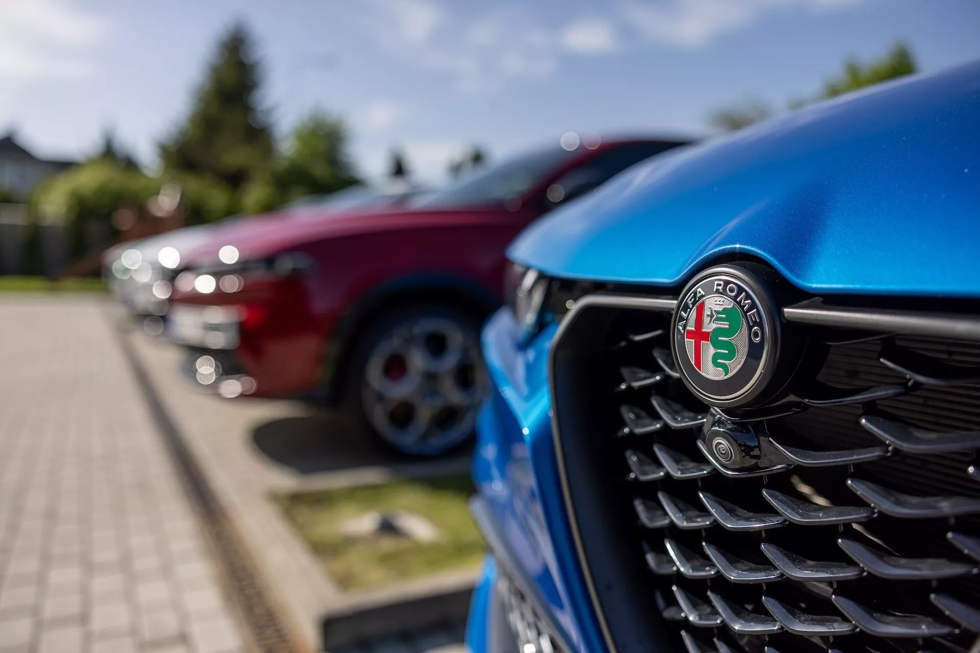 Närbild av den blåa Alfa Romeo Tonale 2022:s frontgrill med fokus på emblemet, med vertikala lister och en suddig bakgrund av andra fordon