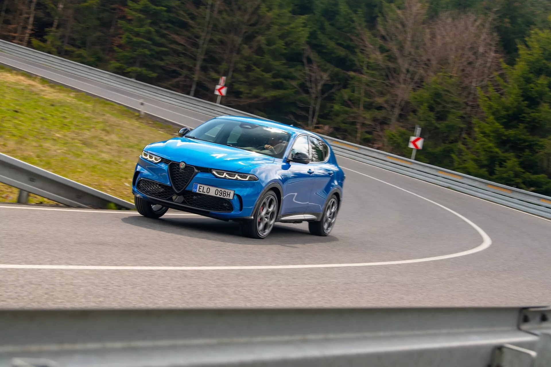 SUV Alfa Romeo Tonale 2022 i rörelse med dynamisk design och LED-strålkastare, stora legeringshjul och sportiga funktioner, fångad från en låg sidovinkel som betonar dess hastighet och glänsande metalliskt blå finish