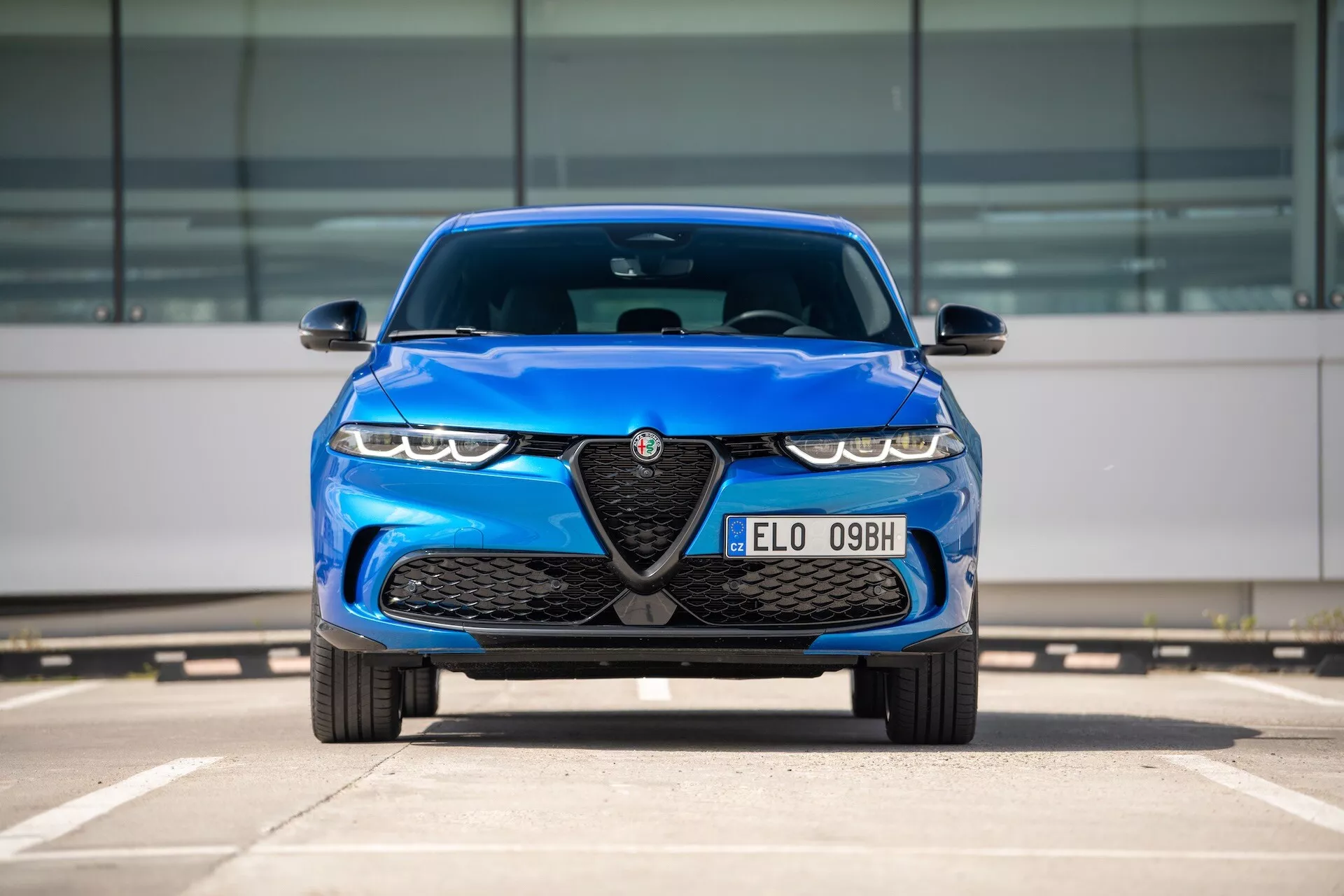 Alfa Romeo Tonale 2022 i blått, främre vy på parkeringsplats som visar grill med emblem, LED-strålkastare och aerodynamiska designfunktioner