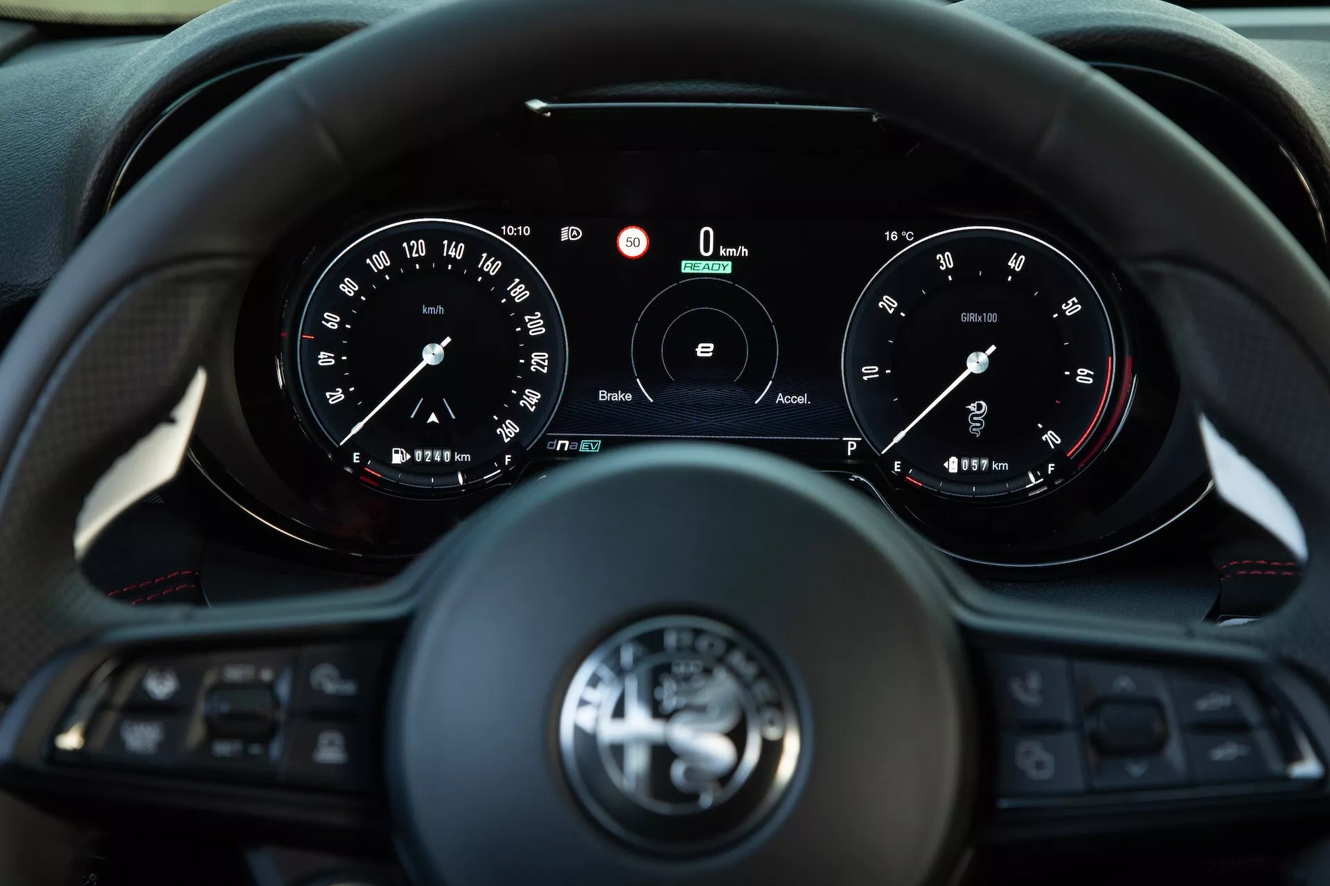 Interiör av Alfa Romeo Tonale 2022 som visar förarens syn på en trespakad multifunktionell ratt och instrumentkluster med analoga mätare och en central digital display som indikerar nollhastighet och varvtal, med teknologier för anslutning och förarassistans
