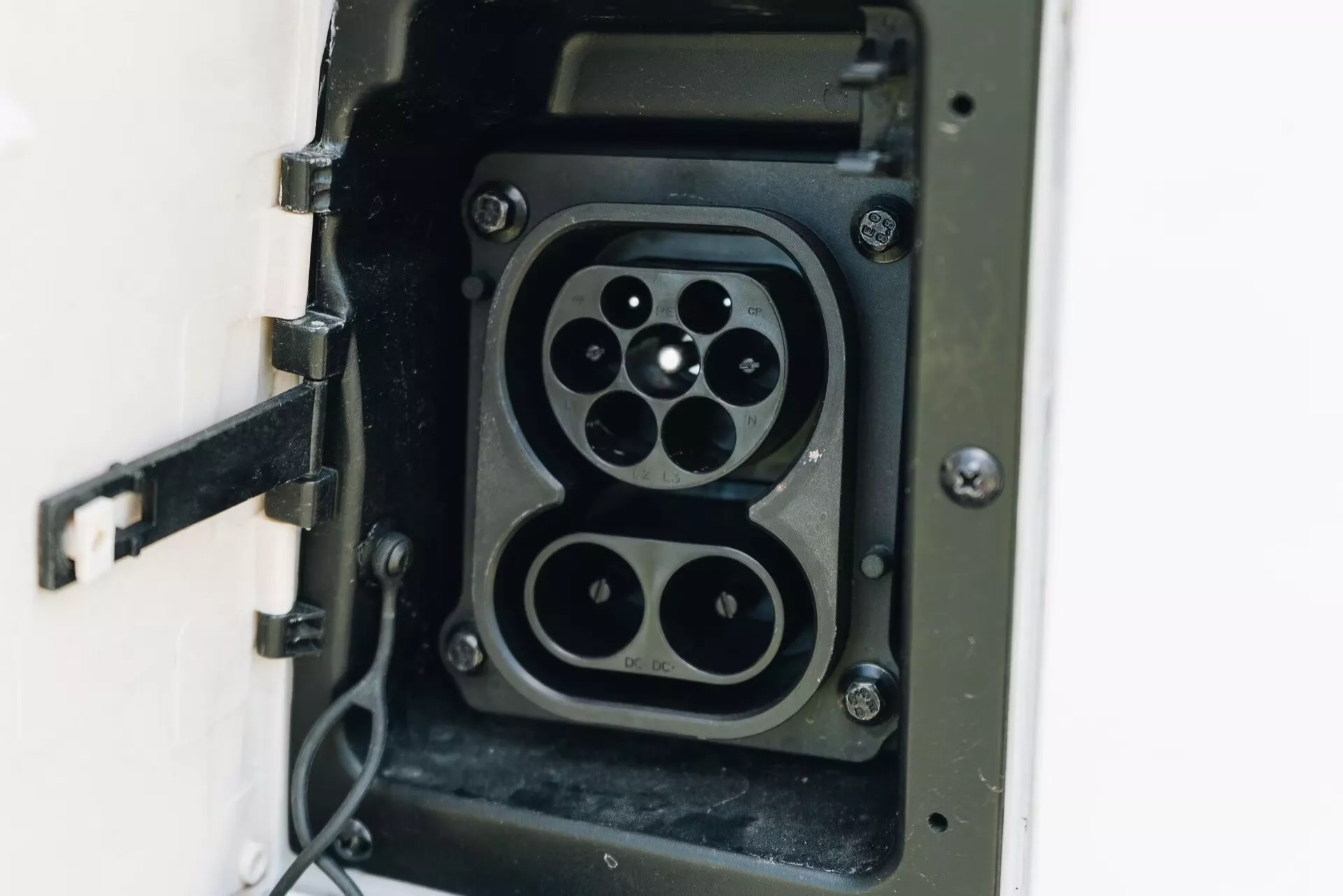 Närbild av ett laddningsuttag för elfordon (EV) som visar två olika plugdesigns inom samma enhet: en Typ 2-kontakt med sju-stiftsarrangemang och en CHAdeMO-plugg med fyra stora stift och en mindre kommunikationsstift, vilket indikerar kompatibilitet för flera EV-laddningsstandarder. Det gångjärnsförsedda locket är öppet och en flexibel kabel är fäst, vilket betonar fokus på EV-infrastruktur, laddningsteknik och hållbar transport.