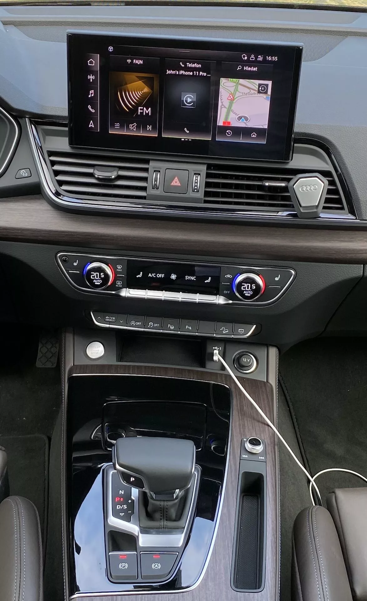 Översiktsvy över Audi Q5 2020 Sportback's mittkonsol och instrumentpanel, som visar detaljerade funktioner som infotainmentskärm, tvåzons klimatanläggning, modern växelväljare med läderöverdrag och lyxiga lädersömmar. Perspektivet belyser den eleganta designen, pianoljusa och metalliska accenter samt avancerad teknologi inklusive trådlös laddningsplatta och körlägesval.