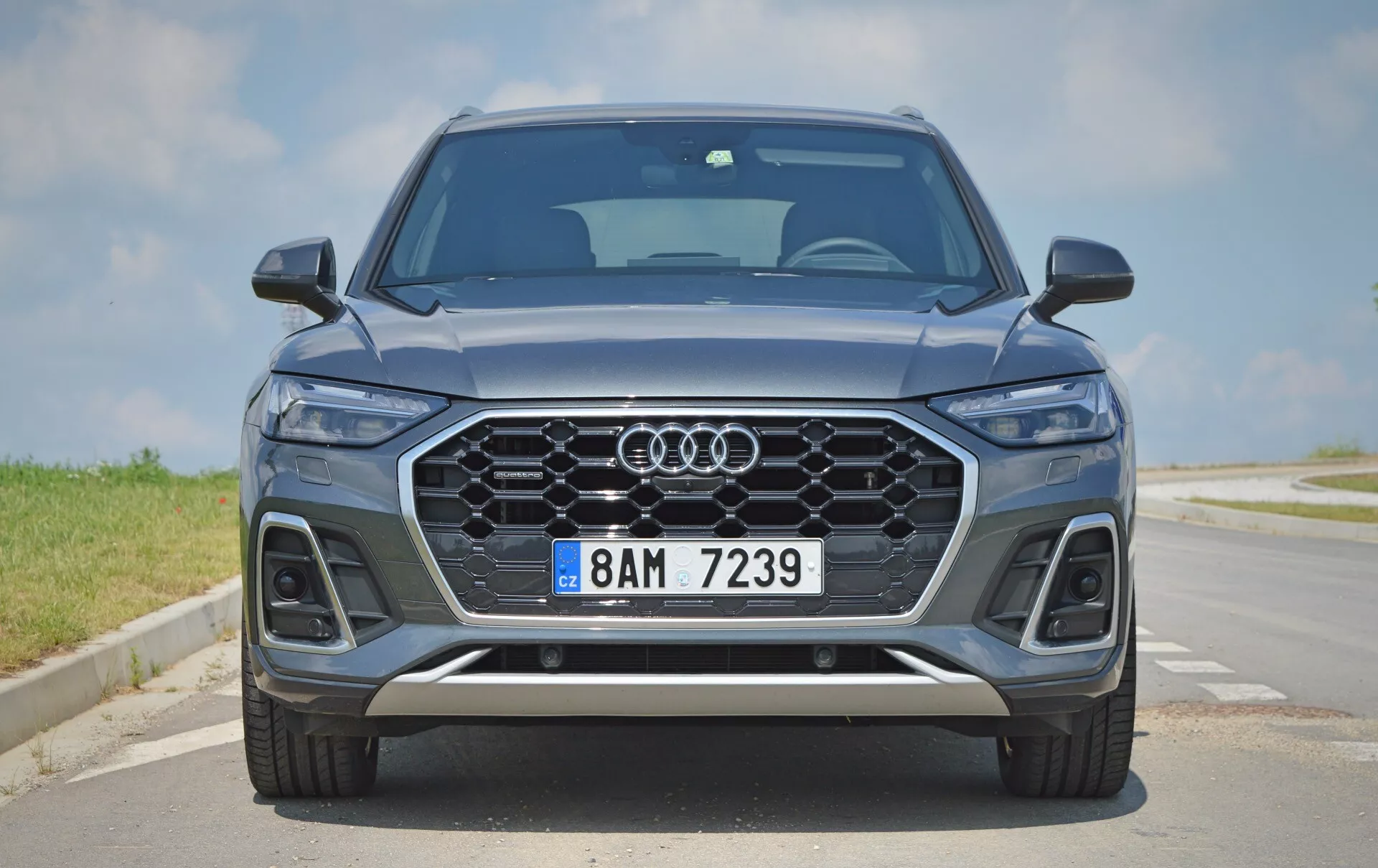 Frontal vy av en modern Audi Q5 2020 Sportback SUV som visar dess eleganta och symmetriska front, med den ikoniska Audi-grillen, LED-strålkastare, parkeringssensorer, metallic blå färg, lättmetallfälgar och silverdetaljer. Scenen är satt på en asfalterad väg under klar himmel.
