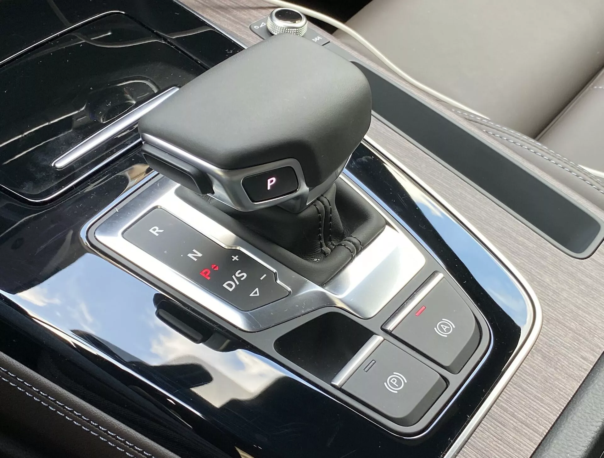 Toppvy av mittkonsolen i Audi Q5 Sportback 2020, som framhäver den raffinerade växelspaken med en automatisk läderklädd växelväljare, upplysta växellägeindikatorer och intilliggande kontrollknappar för automatisk parkeringsbroms och Auto Start/Stop funktion. Konsolen har en pianolackfinish med silverdetaljer, som speglar den lyxiga inredningsdesignen och modern teknologi.