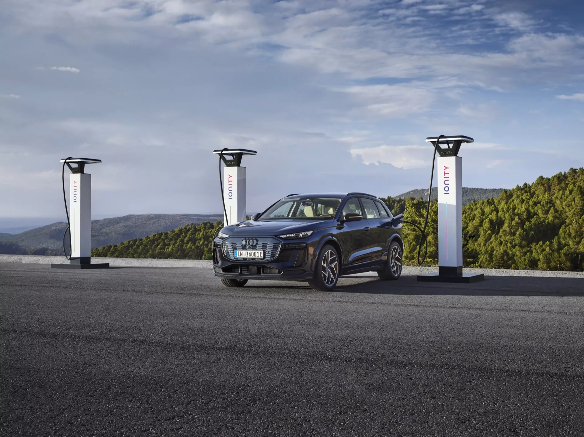 Audi Q6 e-tron SUV 2024 i djup metallisk blå vid en laddstation för elfordon med tre laddare. Bilden fångar bilen från en trekvartsvinkel som visar dess vänstra framsida och del av sidprofilen, vilket framhäver grillen, strålkastarna, hjulen och motorhuven. Den stiliga och moderna elbilen har en sportig och mångsidig design med eleganta, aggressiva strålkastare och aluminiumfälgar, vilket betonar dess avancerade och hållbara bilteknik.