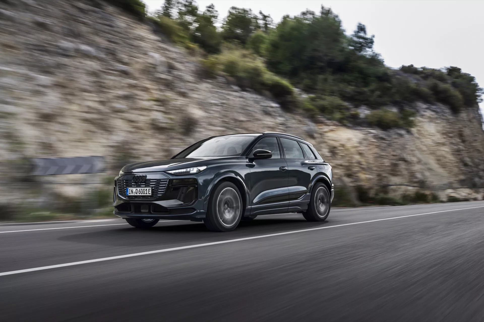 Dynamisk bild av Audi Q6 e-tron 2024 i rörelse från en låg, framåtvänd vinkel, som visar dess slimmade aerodynamiska SUV-design, moderna LED-strålkastare och lättmetallfälgar med rörelse suddighet, vilket antyder prestandakapaciteter på en asfaltväg.