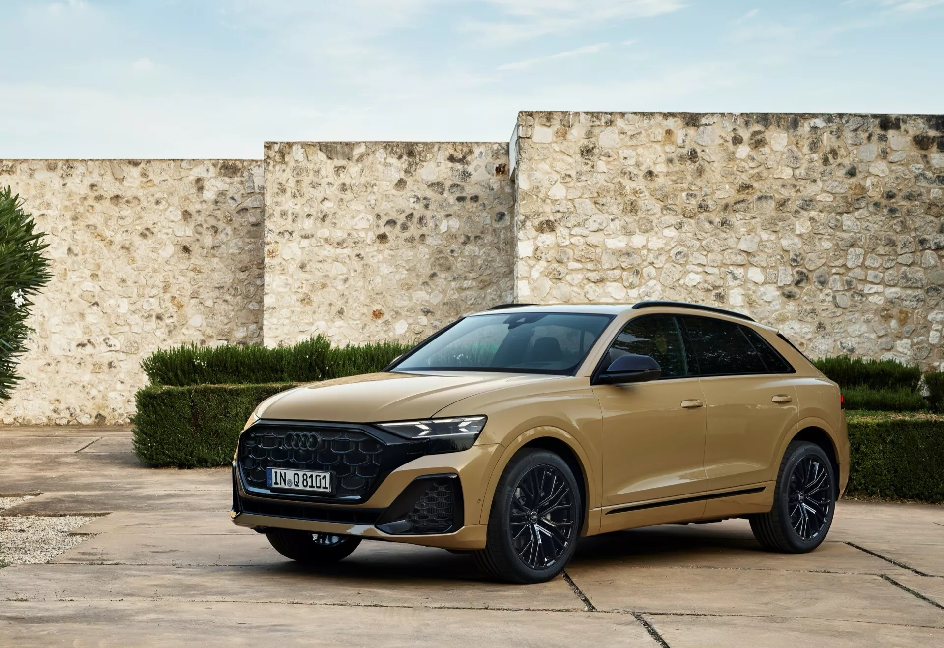 Modernt SUV Audi Q8 2023 (4M-Facelift) i dämpat guld, parkerad på en historisk gård som visar fram grill, eleganta strålkastare och sportig sidoprofil med tekniska egenskaper och lyxiga designelement under naturligt ljus