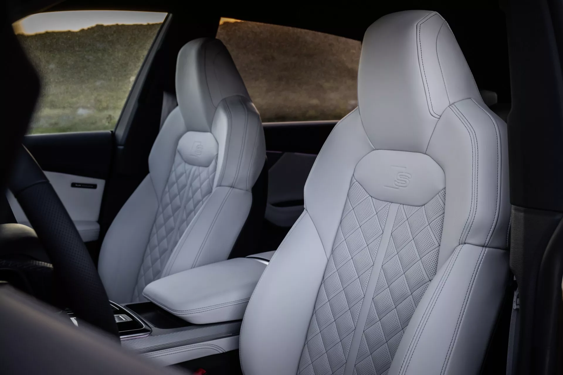 Interiörvy av Audi Q8 2023 (4M-Facelift) som framhäver de lyxiga framsätena med ljusfärgad diamantmönstrad klädsel och präglat Mercedes-Benz-logotyp, med en skimt av högteknologisk mittkonsol från ett avcentrerat bakre perspektiv.