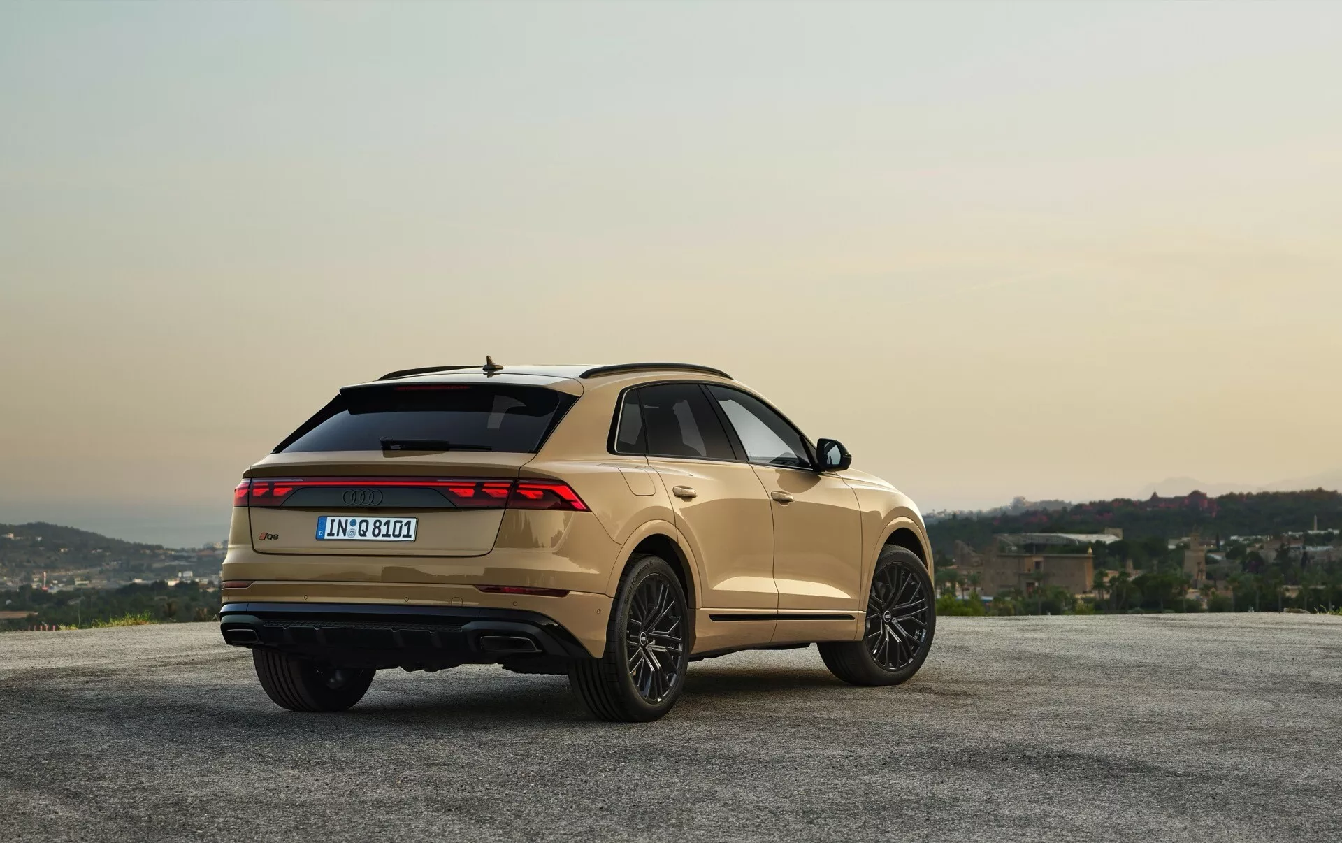 Audi Q8 2023 (4M-Facelift) i metallisk finish parkerad vid naturskönt utsiktsplats med kullar och gryning/skymningshimmel, visar vinkel från tre fjärdedelar bakifrån för design & funktionsvy