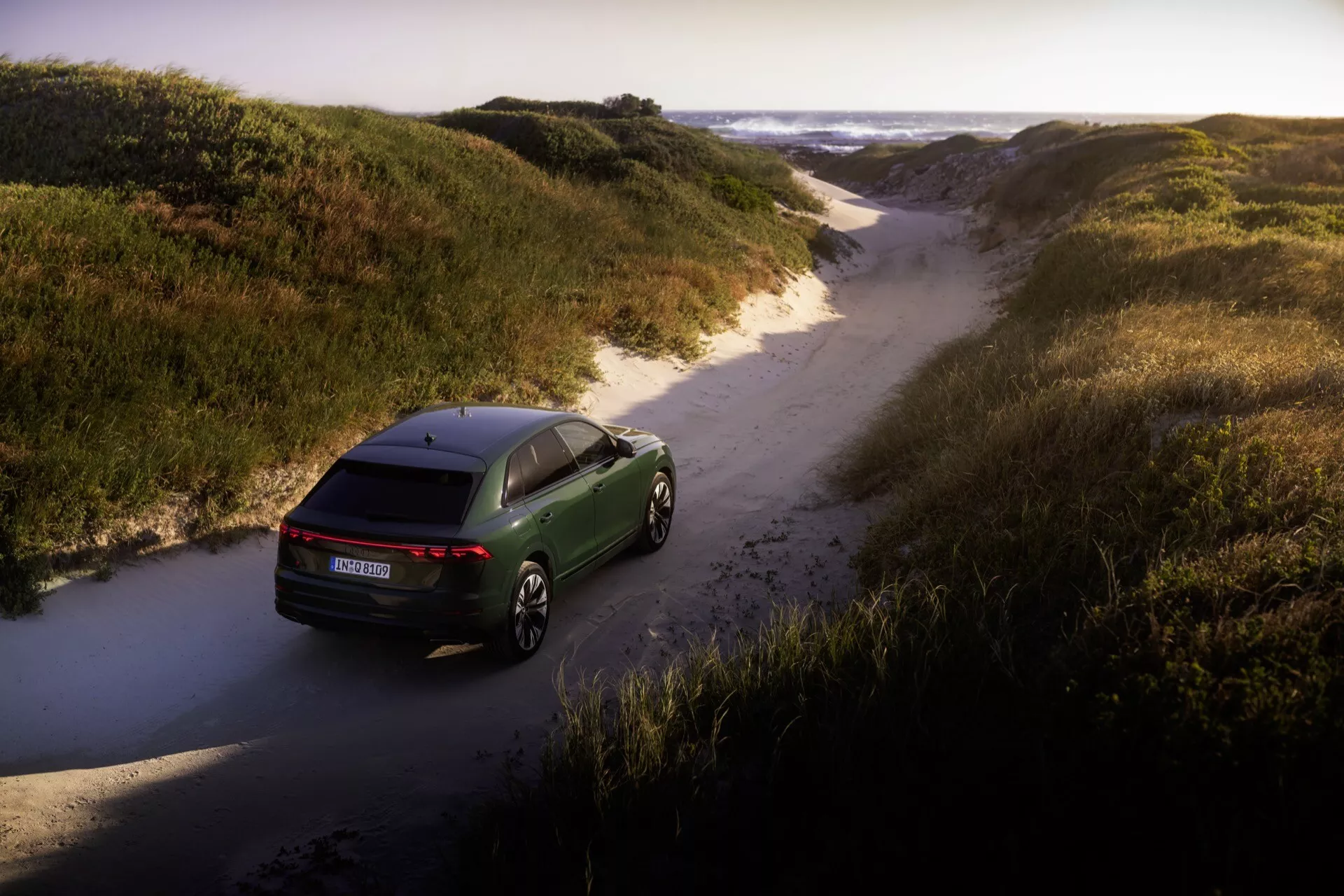 Audi Q8 2023 (4M-Facelift) fångad från ett fågelperspektiv som visar upp sin aerodynamiska design, LED-baklampor och premiumlegeringshjul i en naturlig terränginställning