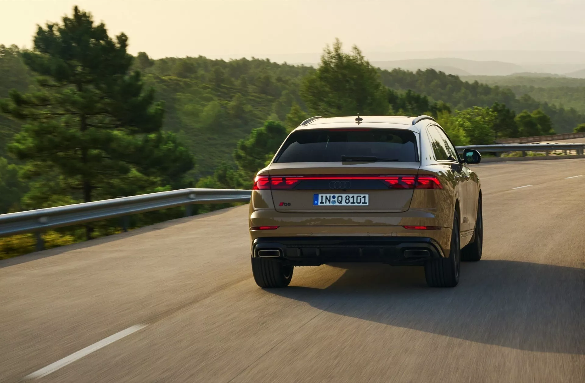 2023 Audi Q8 (4M-Facelift) fångad i en dynamisk bakre trekvartsutsikt medan den kör på en öppen väg, med fullbredd bakljusdesign och dubbla avgastips