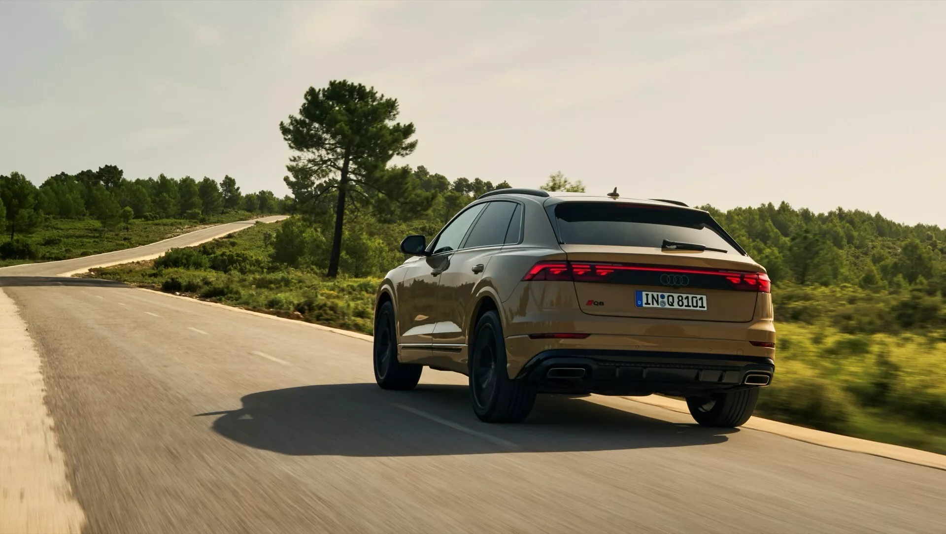 Audi Q8 2023 (4M-Facelift) i rörelse på en kurvig väg, visar dess sportiga bak- och sidoprofiler med LED-ljusstav, dubbelavgas och metallisk finish