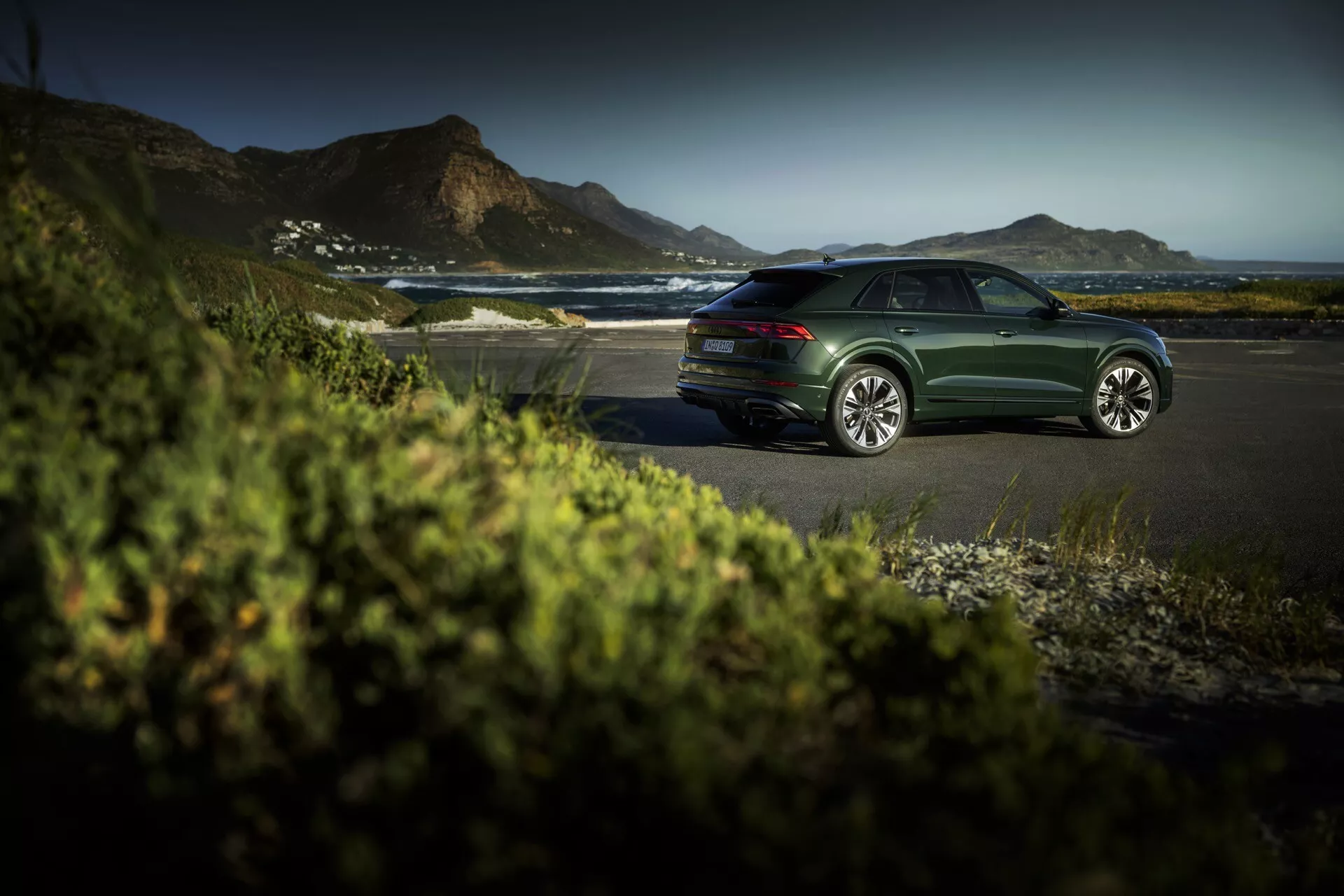 Sedan Audi Q8 (4M-Facelift) i mörkgrönt parkerad på en kustväg under gyllene timmen, visar eleganta designlinjer, flerspakiga aluminiumsfälgar och en lugn lyxig utomhusmiljö