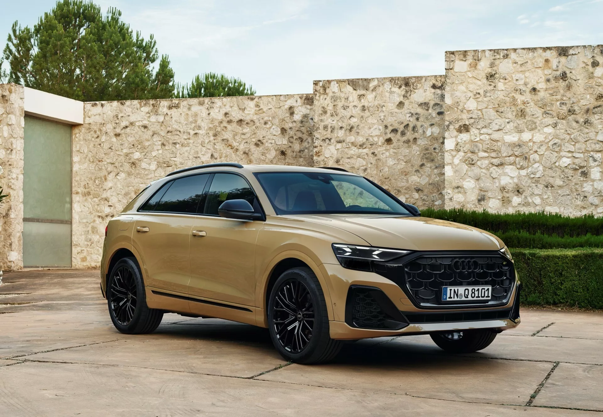 Tre fjärdedels frontvy av Audi Q8 2023 (4M-facelift) i guldnyans, som visar dess aerodynamiska sidoprofil, distinkta grill, LED-strålkastare och lyxiga legeringshjul, parkerad med en lätt vridning mot kameran mot en sofistikerad bakgrund