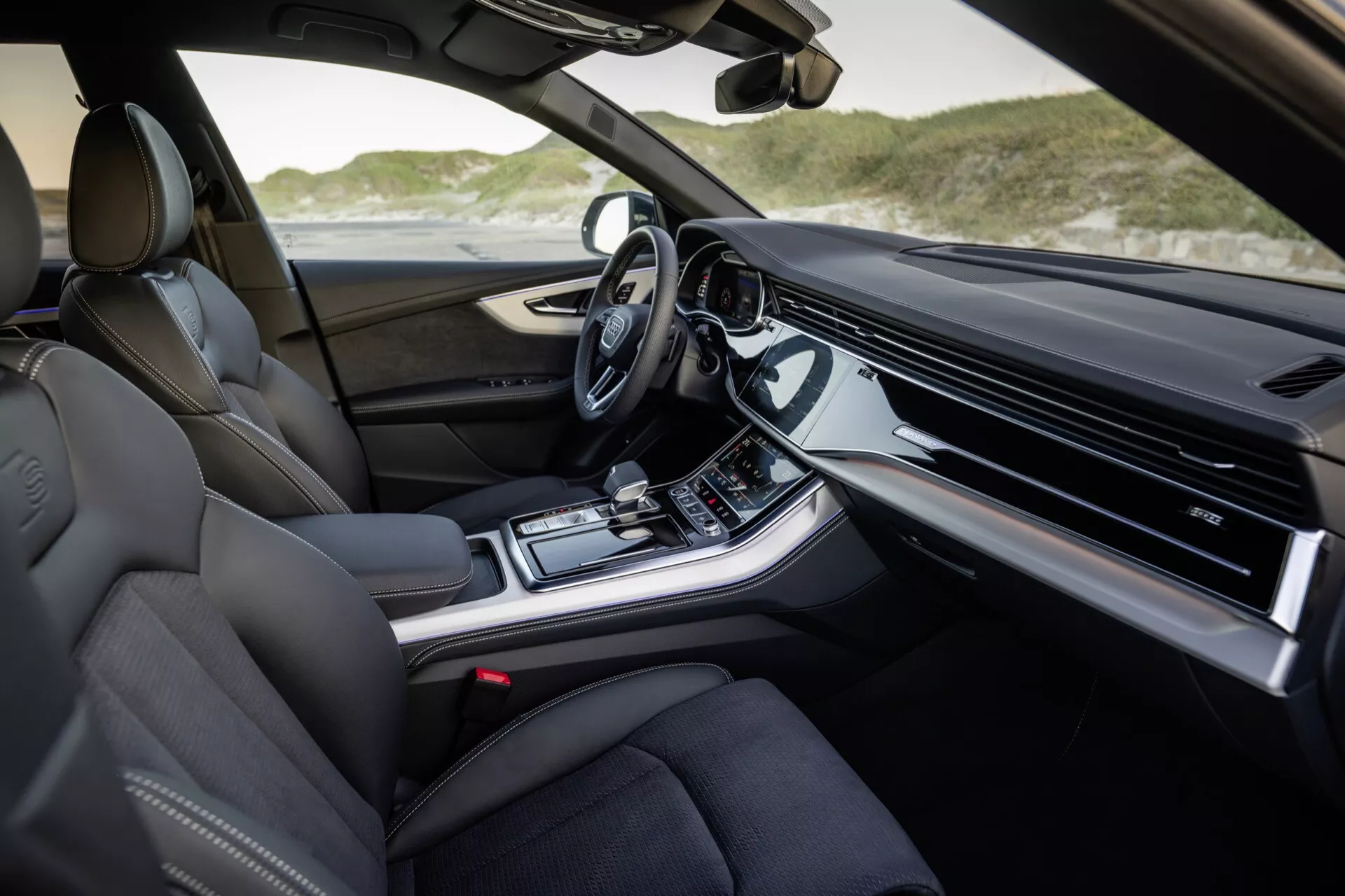Interiörvy av Audi Q8 2023 (4M-Facelift) från passagerarsidan med lyxiga lädersäten, avancerad instrumentbräda med integrerat infotainment-display, mittkonsol med klimatkontroller och körlägesval, modern automatisk växelspak och teknologiskt utrustad ratt