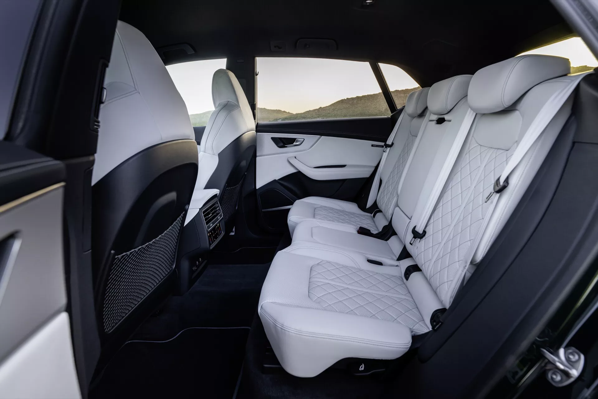2023 Audi Q8 (4M Facelift) lyxigt interiör bakre fackvy som visar premium vit läderimitation med quiltat diamantmönster, justerbara nackstöd, tvåtoniga dörrpaneler med kromaccents, fällbar armstöd, luftkonditioneringsventiler för bakre passagerare och rymlig benutrymme.