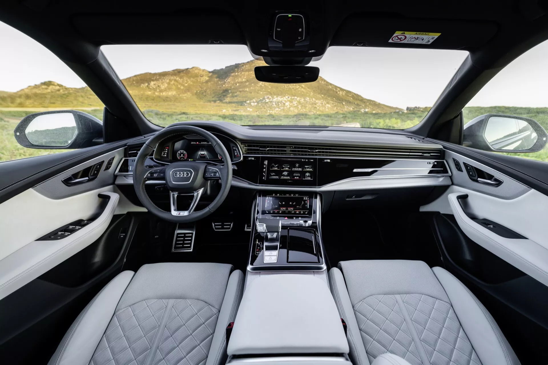 Interiörvy av Audi Q8 2023 (4M-Facelift), med fokus på förarhytten från ett förstapersonsperspektiv, inklusive den sportiga multifunktionsratten, digitala instrumentklustret, breda infotainmentskärmen, ljusfärgade lädersäten med quiltat diamantmönster och högkvalitativa inredningsdetaljer.