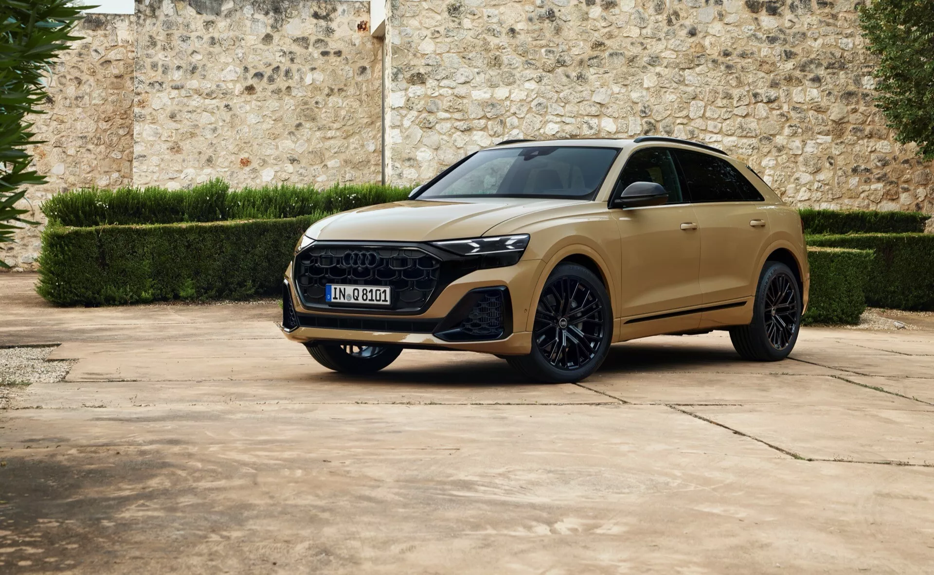 2023 Audi Q8 lyxig crossover SUV i ett tre fjärdedels framtitt parkerad på beläggning med en gammal stenmur i bakgrunden, med snygga LED-strålkastare, framträdande hexagonal grill, skulpterade huvar, stora legeringshjul och möjlig panoramatak.