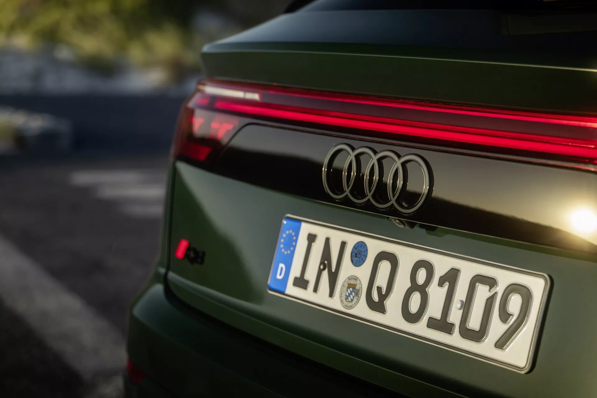 Närbild på baksidan av en grön Audi Q8 2023 4M-Facelift som visar Audi-emblemet, horisontella LED-ljusstripor, europeiskt registreringsskylt från Ingolstadt och sportigt spoilerläpp, med detaljerad design av bakluckan och polerad metallisk finish.