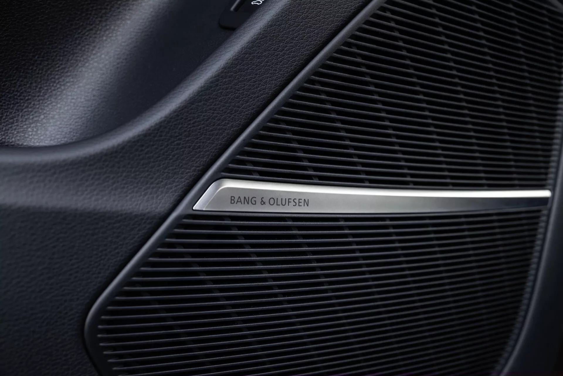 Närbild av Bang & Olufsen högtalargaller i interiören av Audi Q8 2023 (4M-Facelift), som visar det fina meshmönstret av det premium ljudsystemet och den polerade metalliska logotypen på en svart bakgrund.