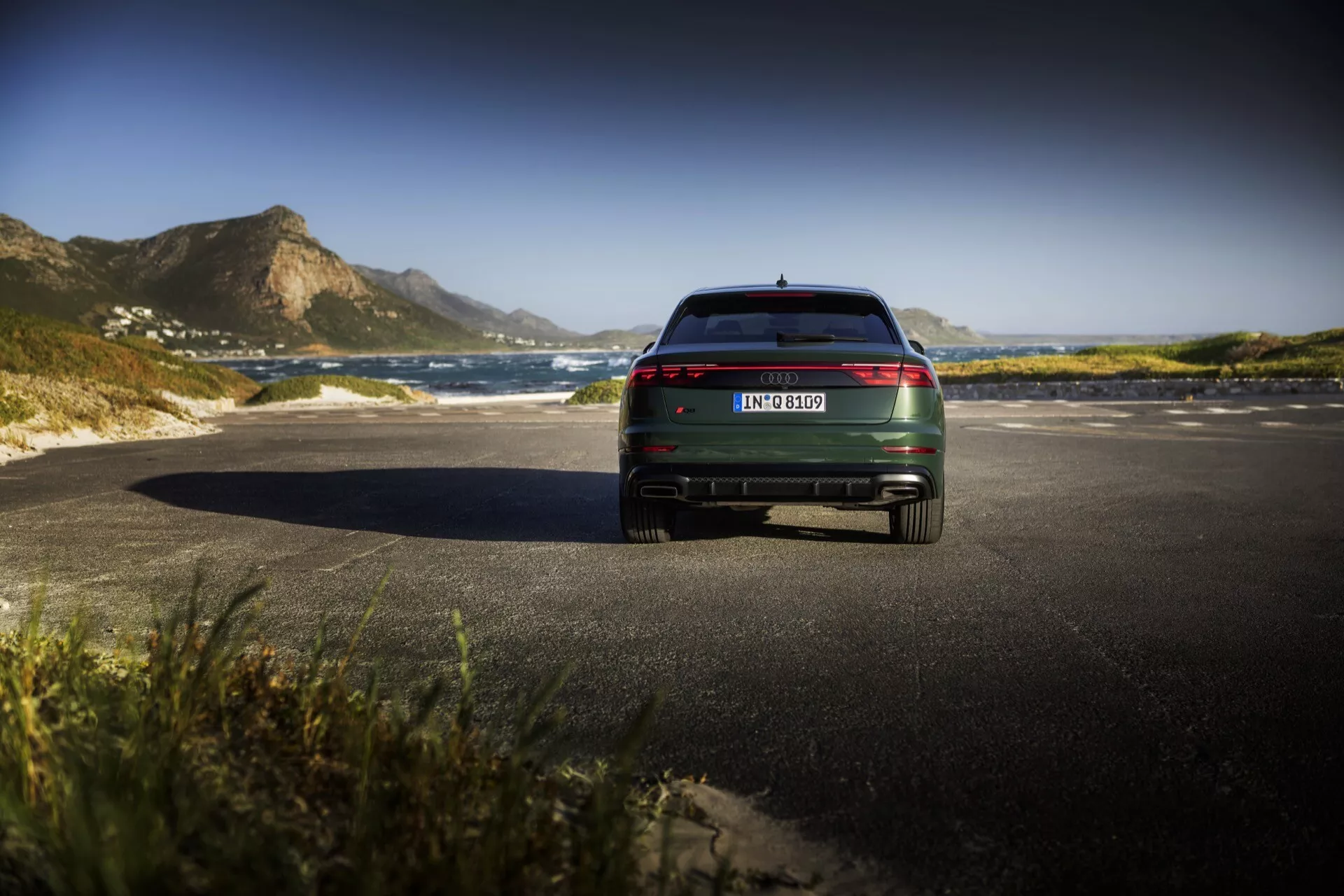 Baksida av Audi Q8 4M Facelift modell 2023, som visar LED-bakljus, kromdetaljer och dubbla avgasutsläpp på en scenisk kustväg