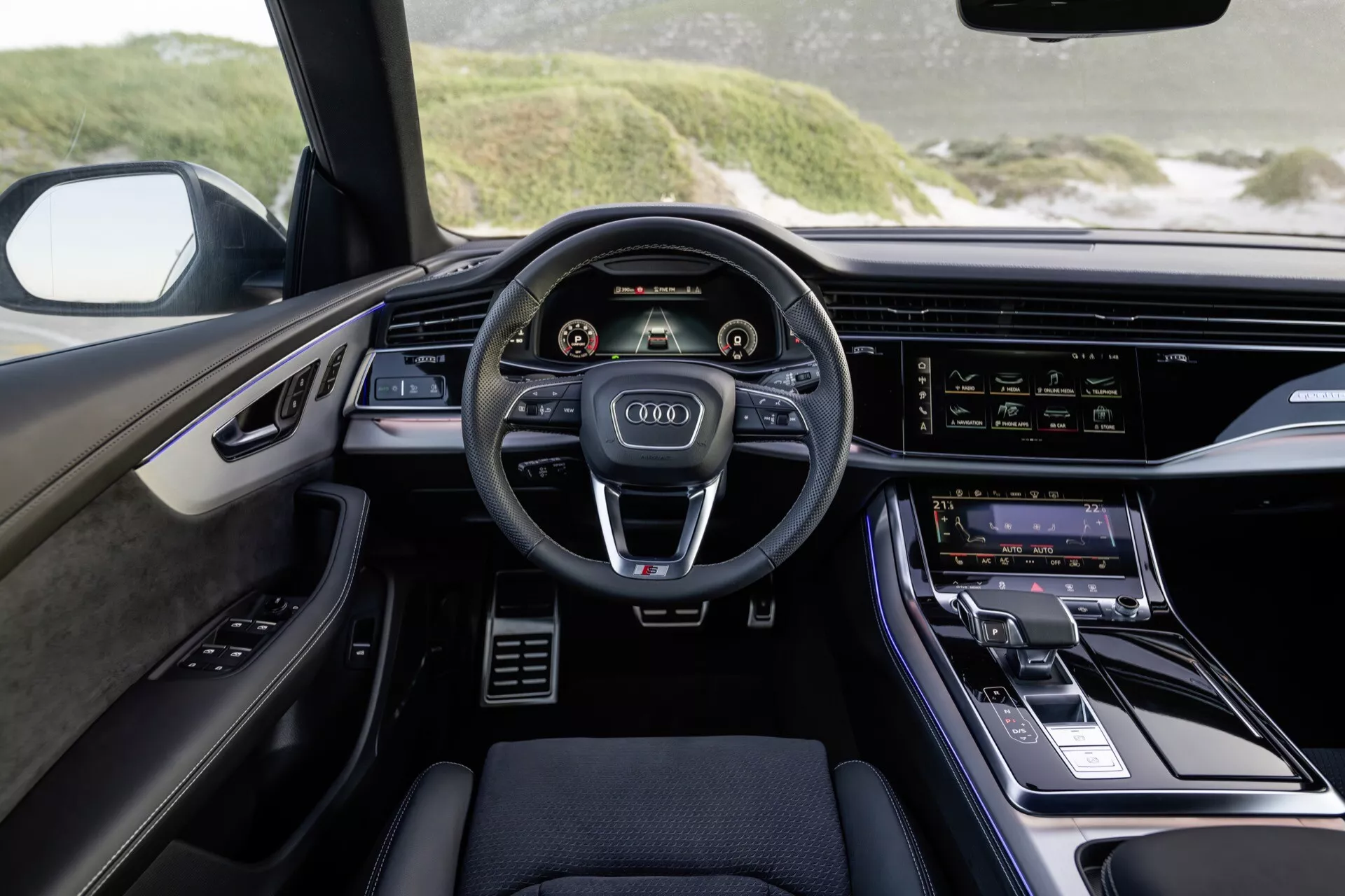 Interiörvy av Audi Q8 2023 (4M-Facelift) från förarens perspektiv som framhäver den moderna instrumentpanelen, tre-ekrad ratt med kontrollknappar, dubbla digitala displayer för instrumentkluster och infotainmentsystem, samt lyxiga designaccent.